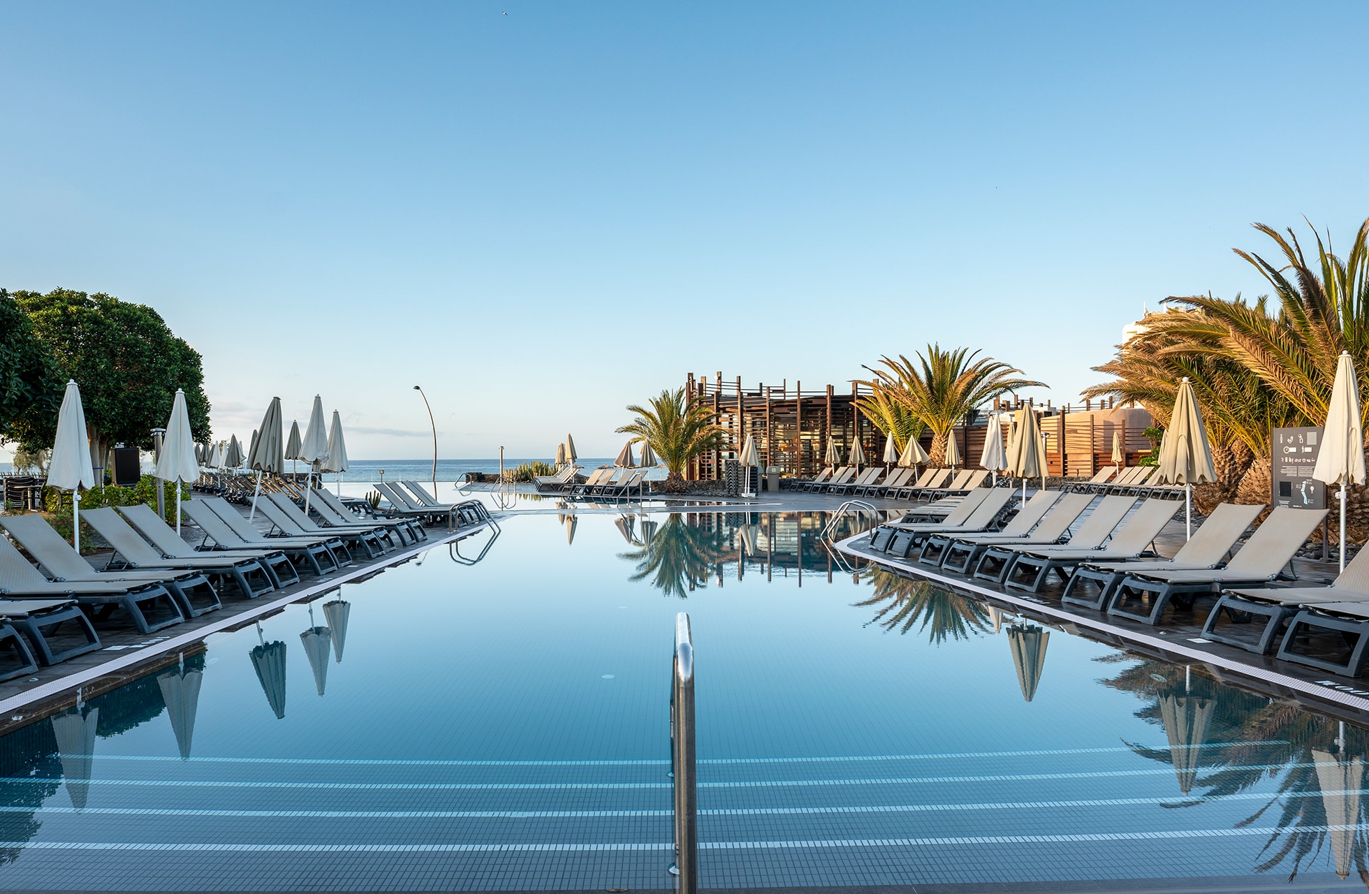 pitkä hotelliallas barceló tenerifessä, aurinkotuolit ja palmut reunustavat allasta, meri näkyy taustalla