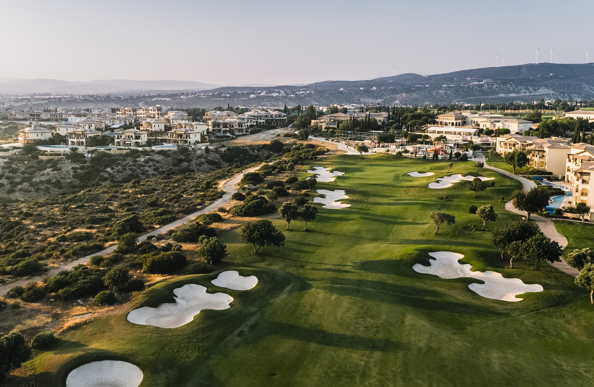 luftfoto av aphrodite hills golfbane med velstelte fairwayer, sandbunkere og omkringliggende bebyggelse i kupert landskap