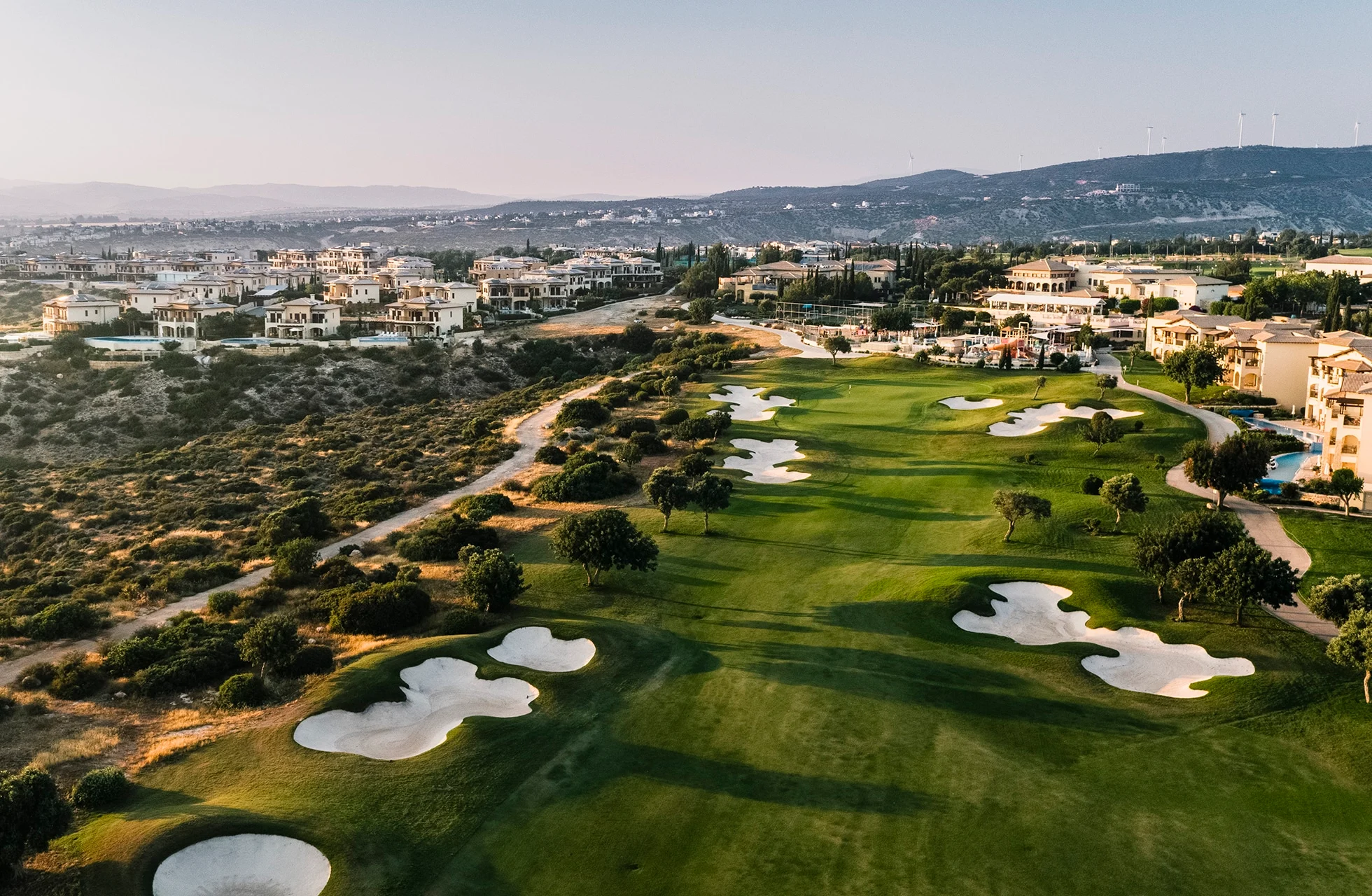 luftfoto av aphrodite hills golfbane med velstelte fairwayer, sandbunkere og omkringliggende bebyggelse i kupert landskap