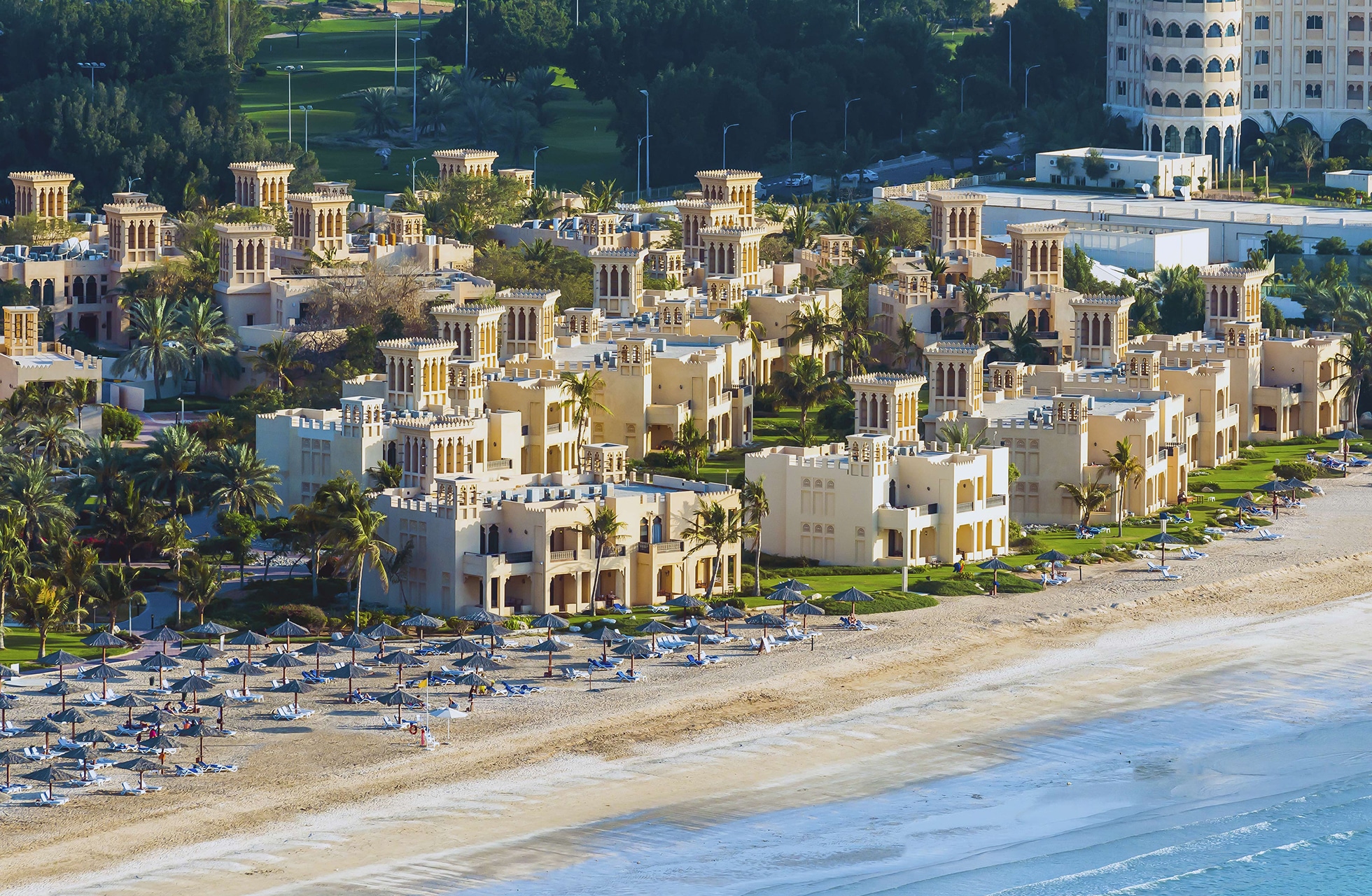 flyfoto av hilton al hamra beach & golf resort med lave villaer, palmer og privat sandstrand langs kysten.