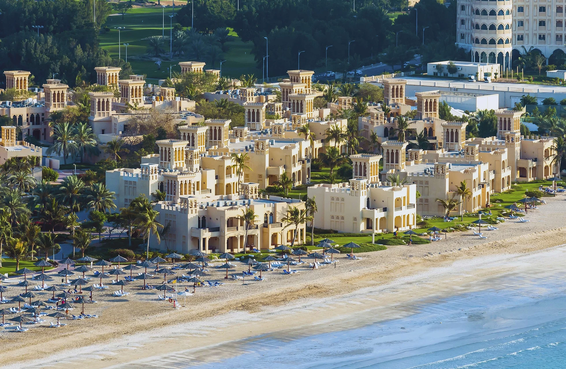 flyfoto av hilton al hamra beach & golf resort med lave villaer, palmer og privat sandstrand langs kysten.