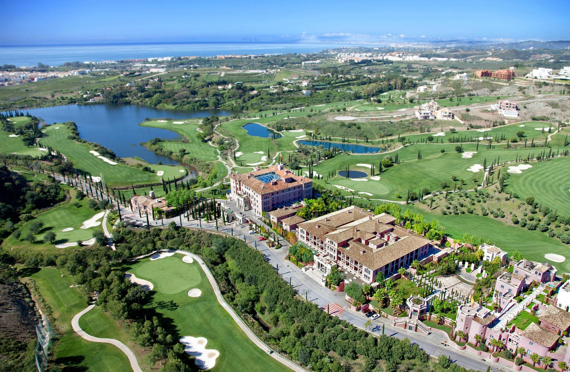 flyfoto av villa padierna golf med resortbygning, golfbaner, vannpartier og kupert landskap, med havet i bakgrunnen i klart dagslys