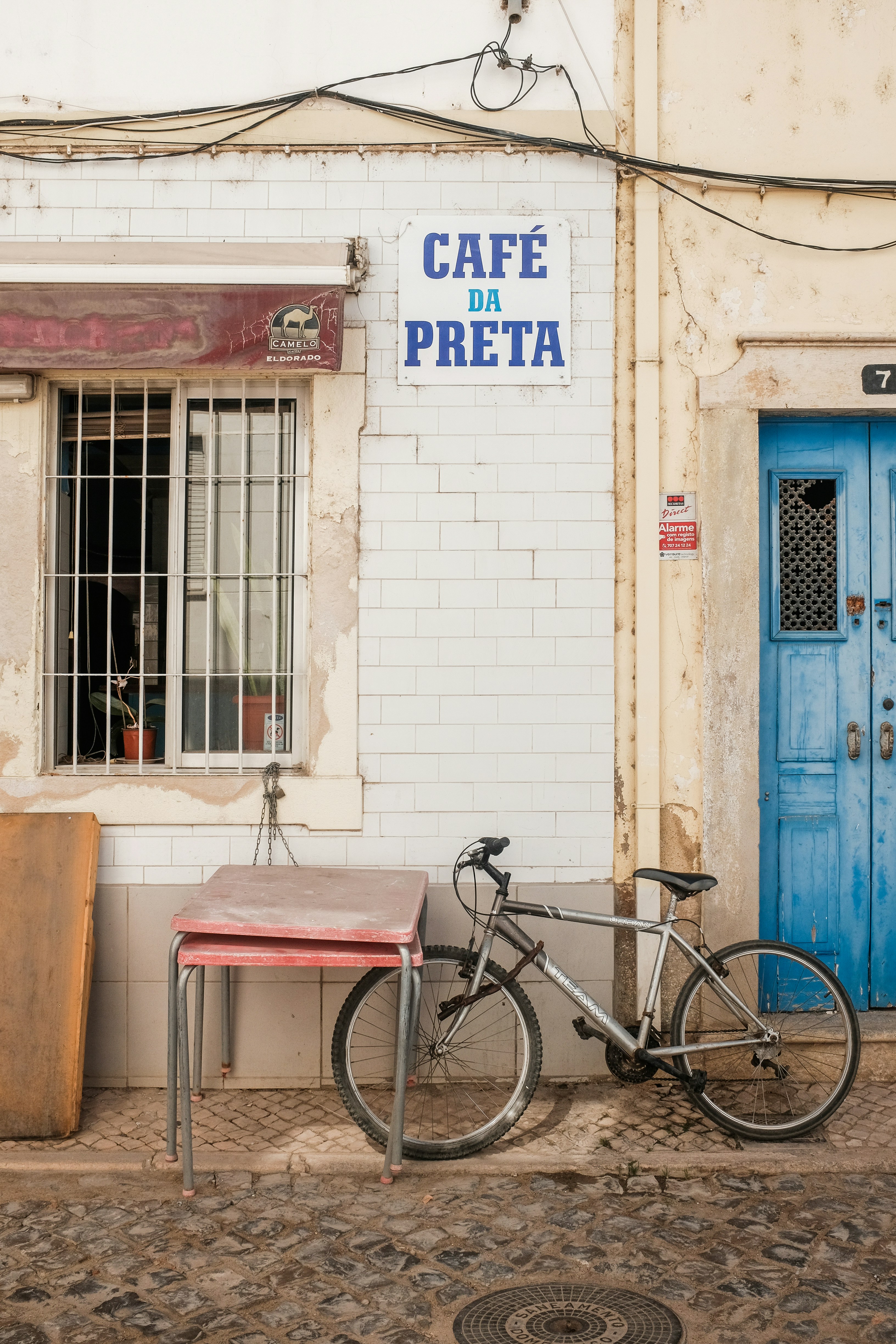 en sykkel står lent mot en lys mur utenfor et kafé med blå dør og et enkelt bord ved siden av