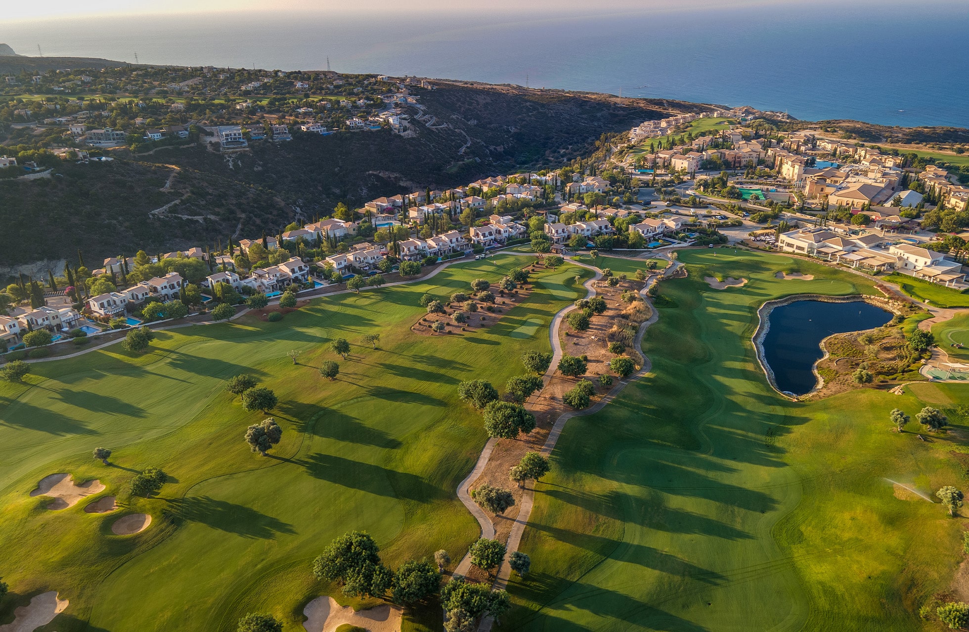 flyfoto av aphrodite hills golf med fairways, boligområde og havet i bakgrunnen