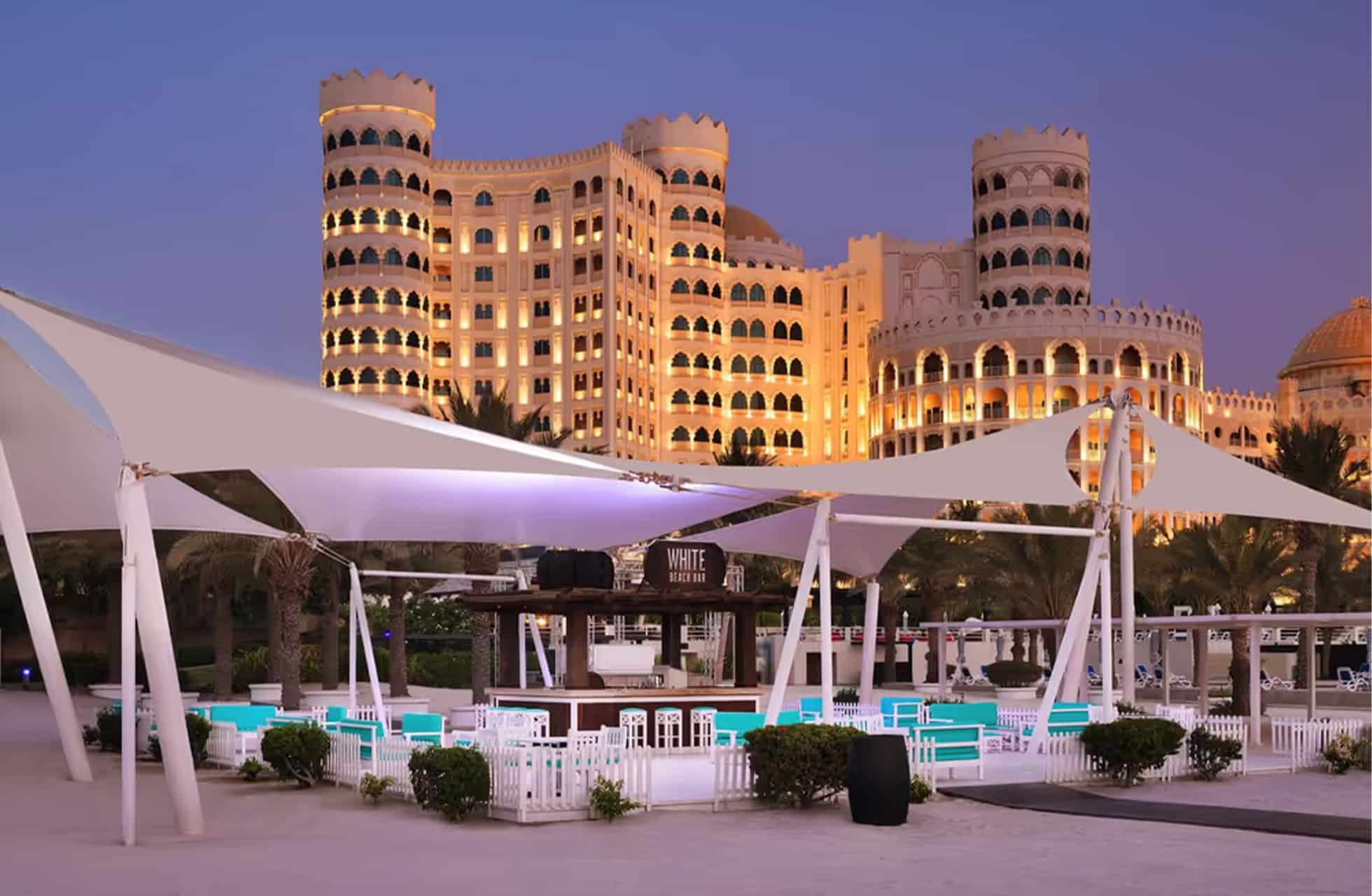 strandrestaurant ved al hamra residence i skumringslys med seilduktak, dekkede bord og opplyst hotellbygning i bakgrunnen