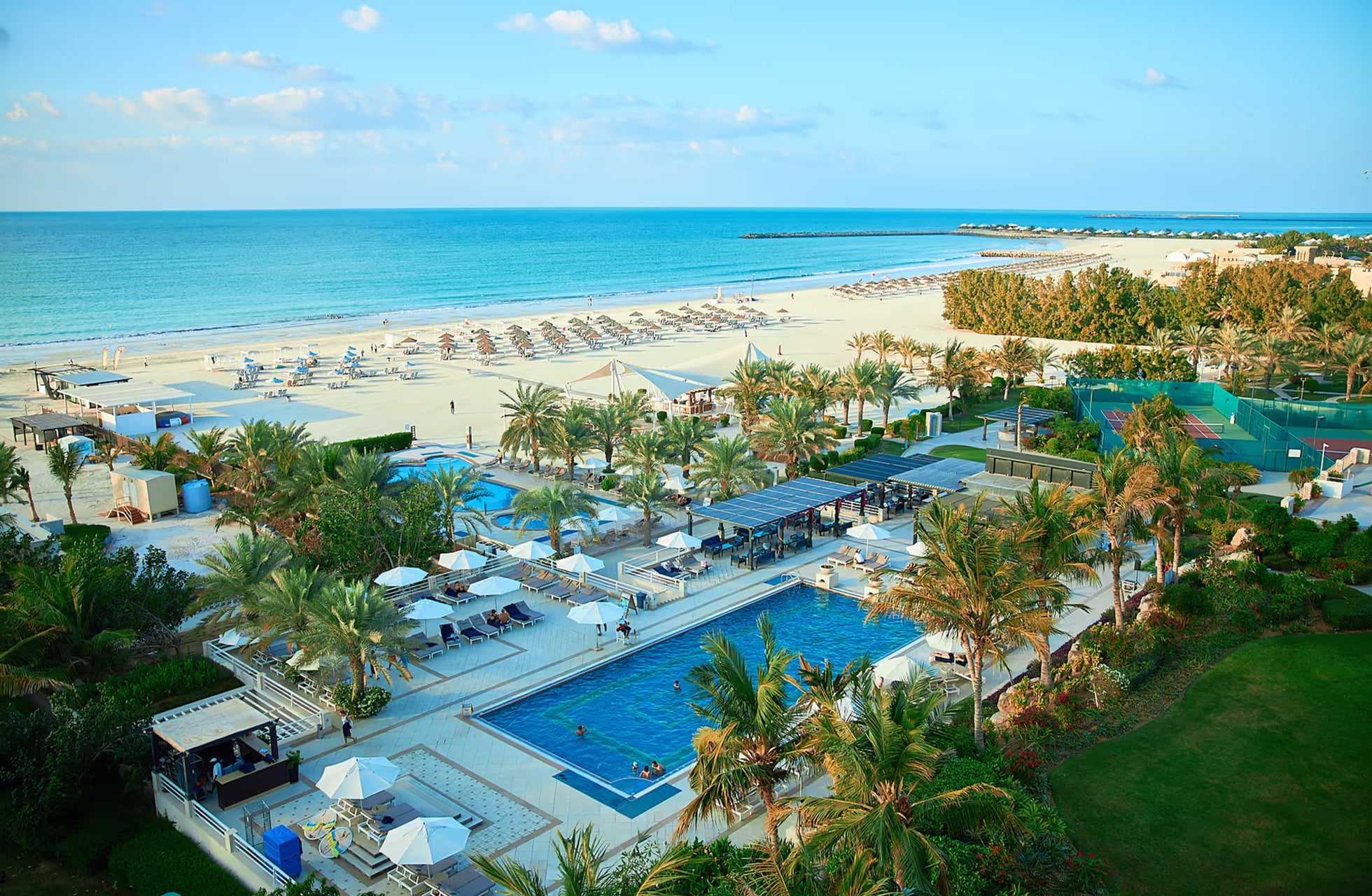 oversiktsbilde av bassengområde ved hilton al hamra beach & golf resort med palmer, solsenger og sandstrand langs havet.