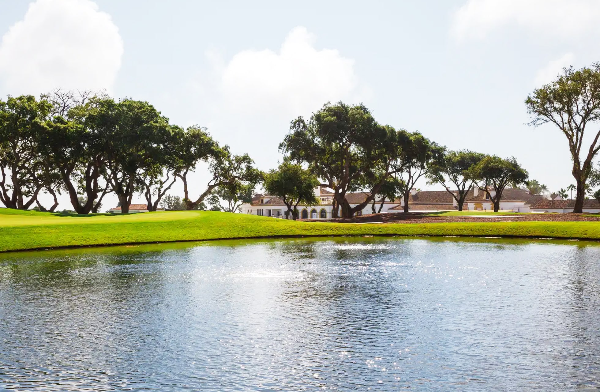 vannhinder foran golfgreen og fairway på san roque new course, omgitt av trær og bygninger i lyst dagslys