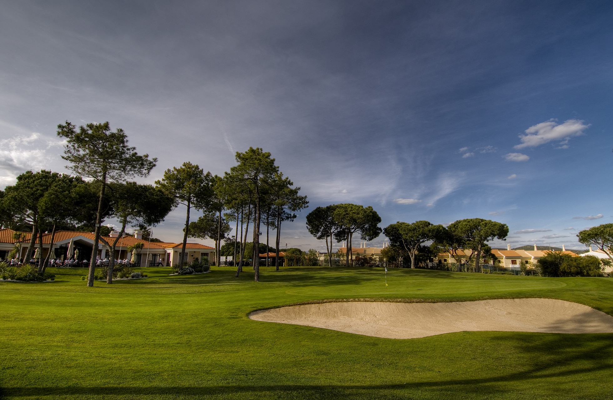 bred fairway med bunker og pinjetrær nær resortbebyggelse på vila sol golfbane.