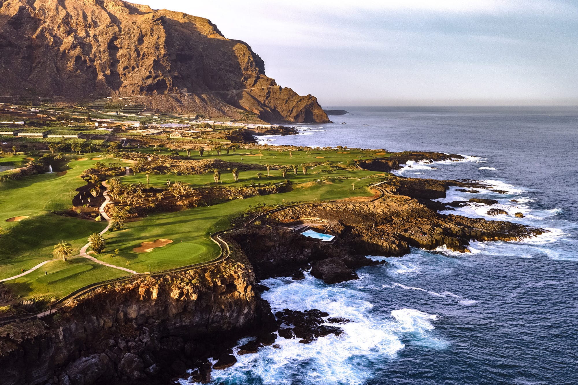 kystnær utsikt over buenavista golf med grønne fairwayer på klipper ved atlanterhavet og fjell i bakgrunnen