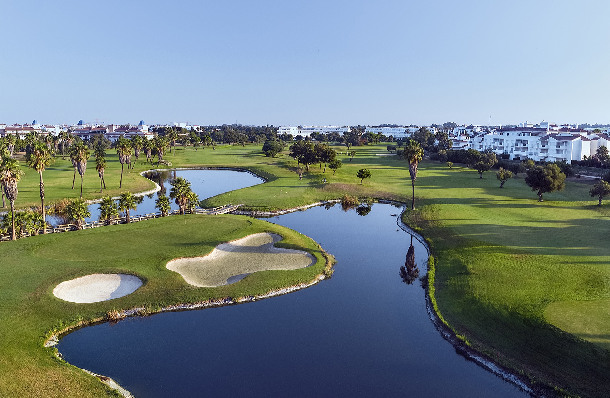 Luftfoto av golfbane med innsjøer, bunkere og palmer rundt greenen og fairwayen.