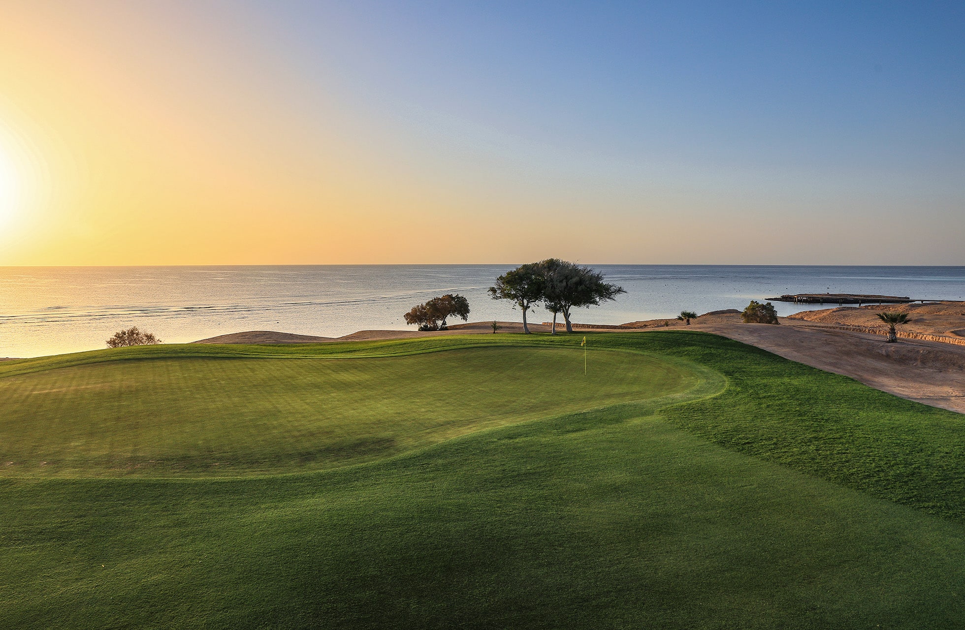 golfgreen ved kysten med flagg på hullet, grønt gress i forgrunnen og havet i bakgrunnen i varmt kveldslys