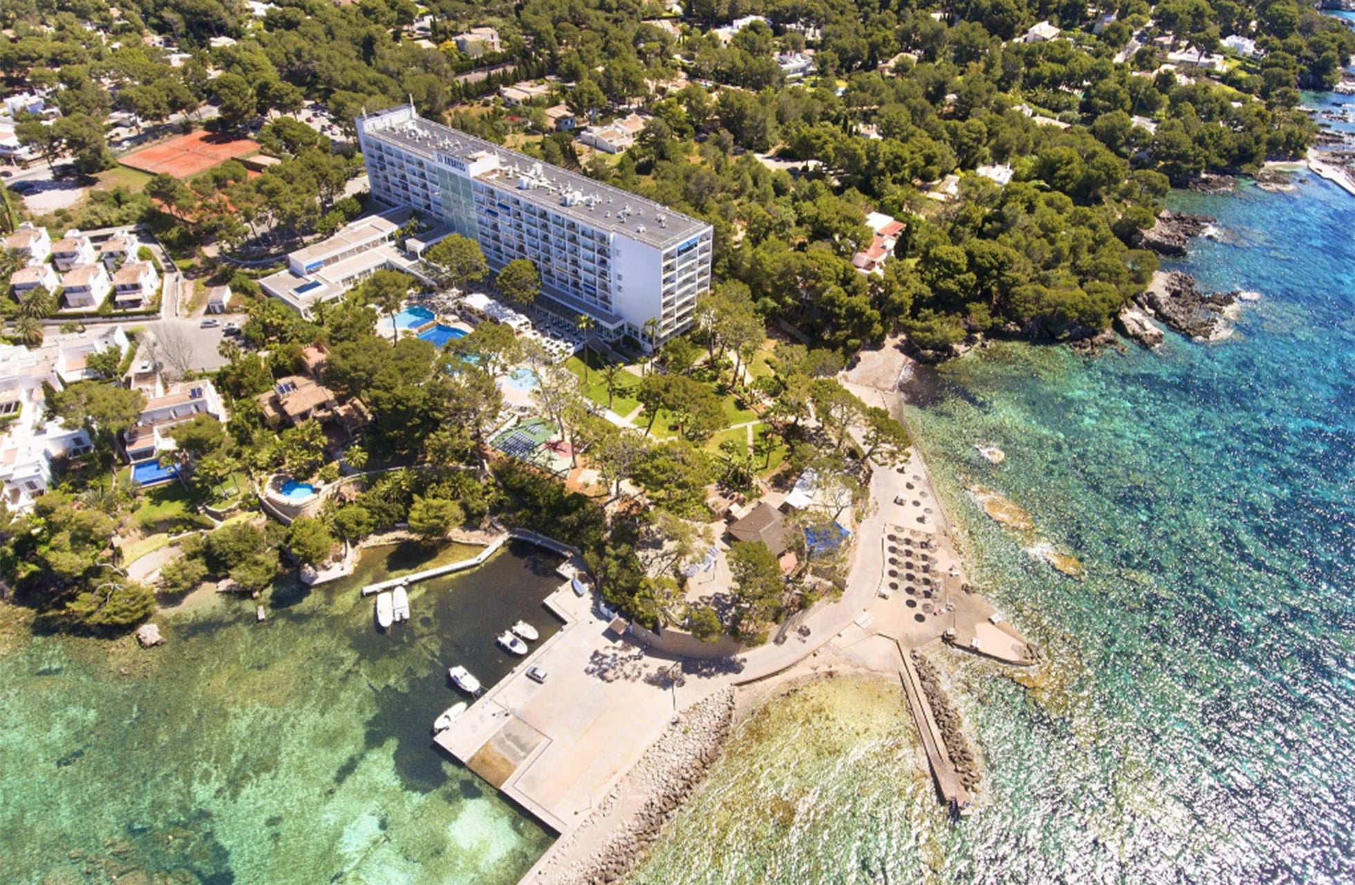 flyfoto av eurotel punta rotja ved kysten med hotellbygning, grøntområder, bassengområder og badeplass ved klart turkist hav i dagslys