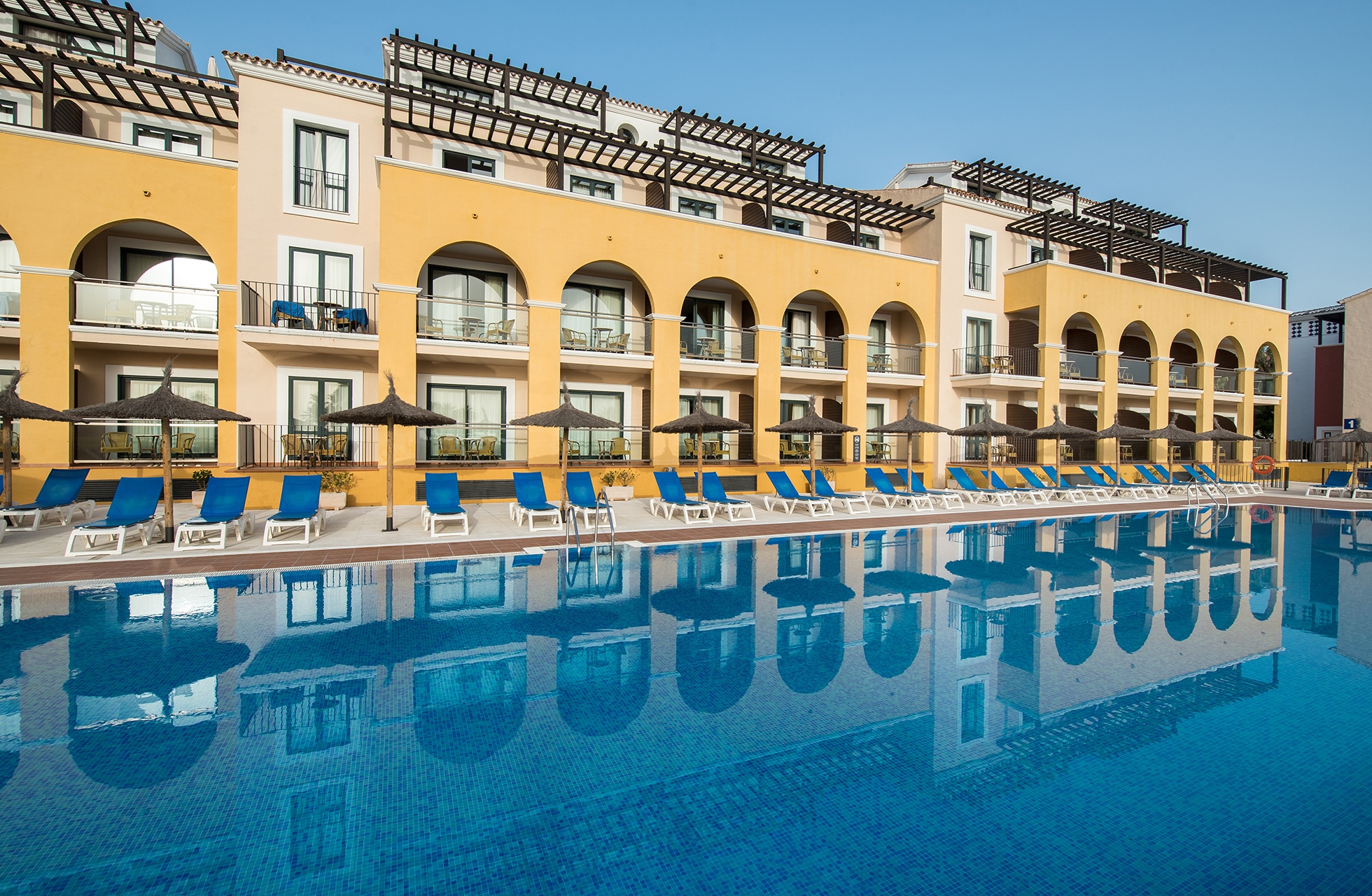 Utendørsbasseng med solsenger foran hotellbygningen på Barcelo-Costa-Ballena-Golf-Spa.