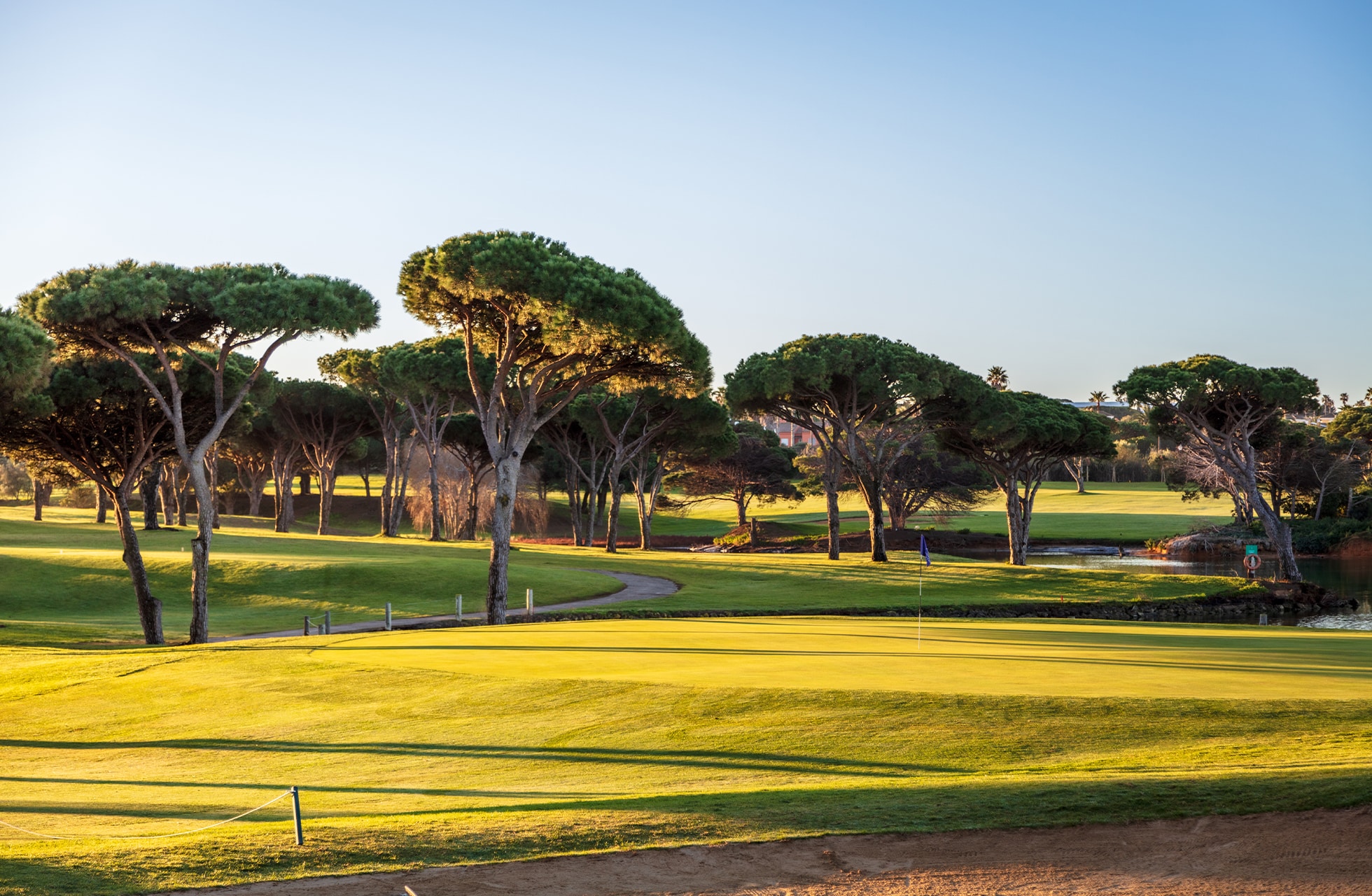 velstelt golfbane i parklandskap med fairway og green, omgitt av karakteristiske trær i varmt kveldslys