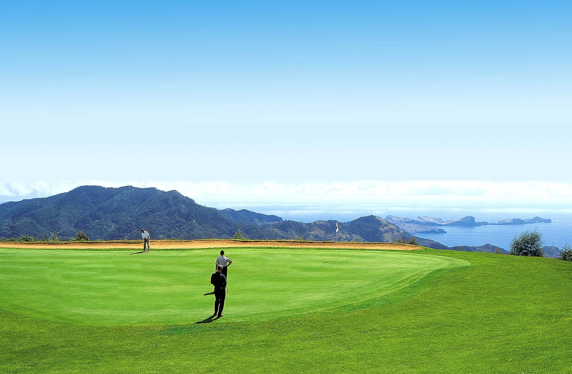 to golfspillere på greenen med utsikt mot fjell og øyer