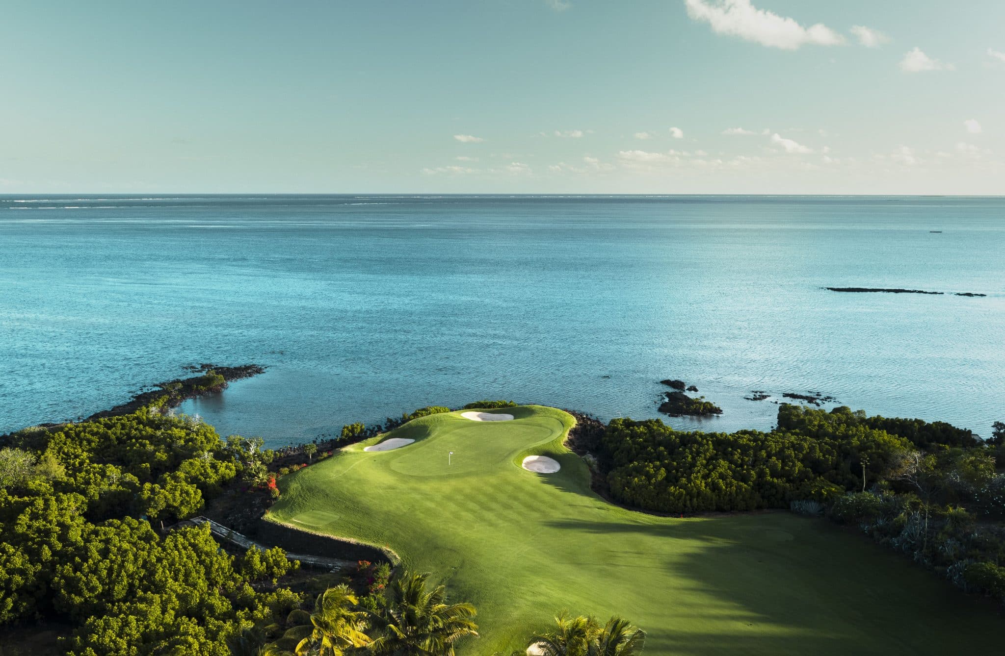 luftfoto af et golfhul på anahita golf club mauritius med green og sandbunker tæt på havet og omgivet af grøn beplantning
