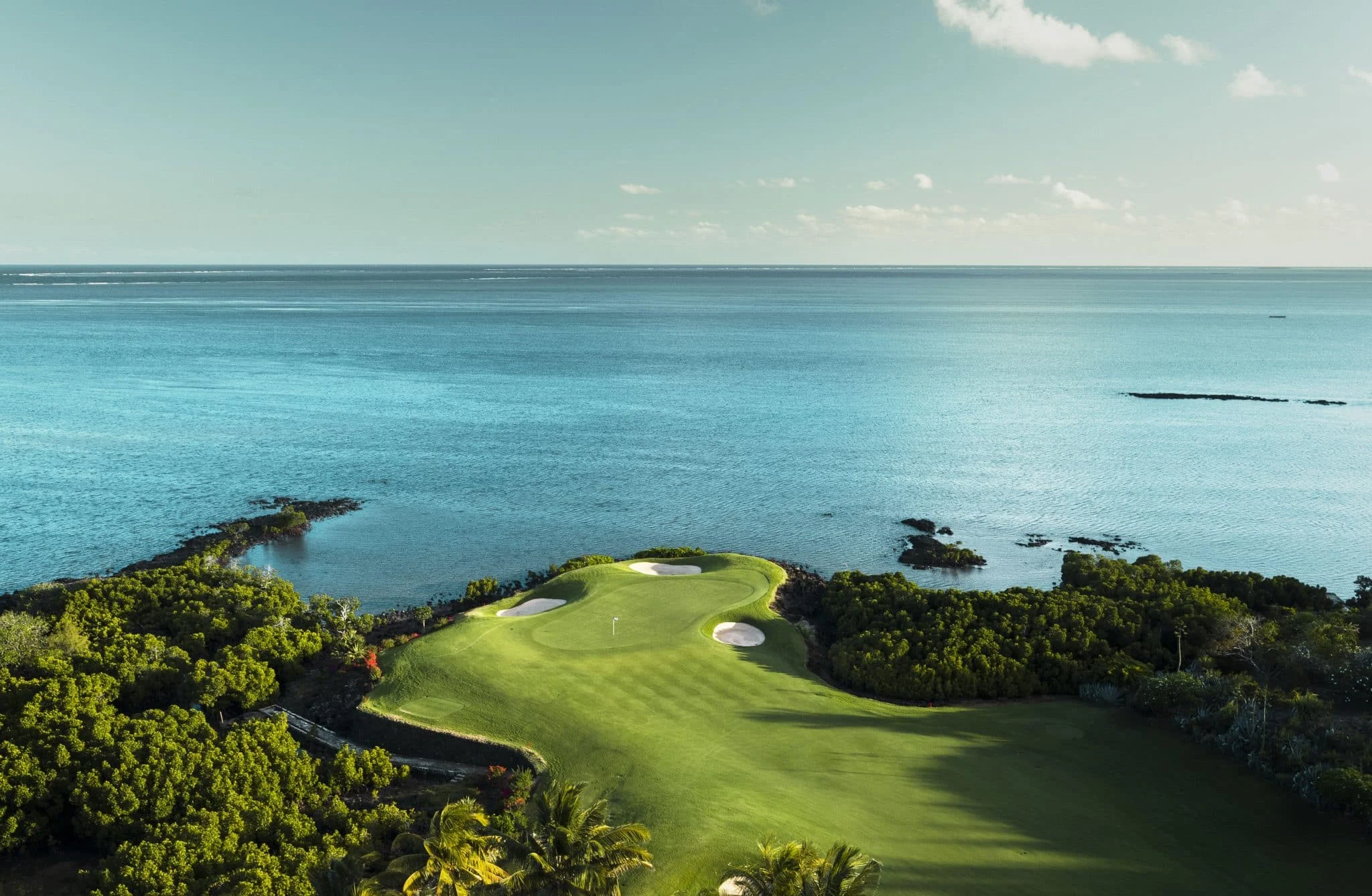 luftfoto af et golfhul på anahita golf club mauritius med green og sandbunker tæt på havet og omgivet af grøn beplantning