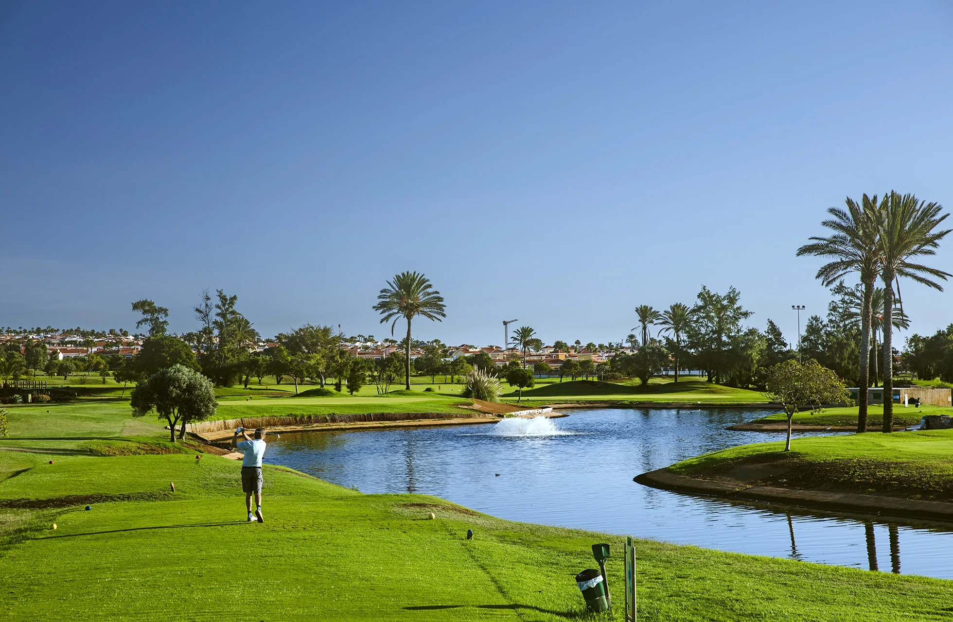 golfspiller, der slår fra tee på fuerteventura golf, med vandhazard foran fairway og green i åbent parklandskab i dagslys