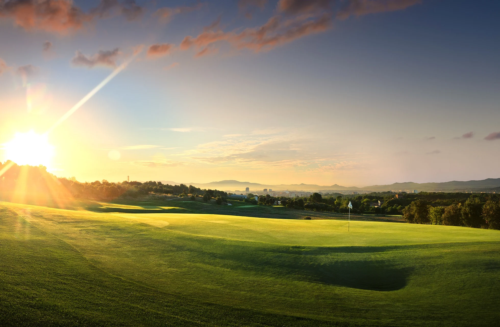 en velstelt golfgreen med flagg i kveldslys, omgitt av åpent landskap og lave åser.