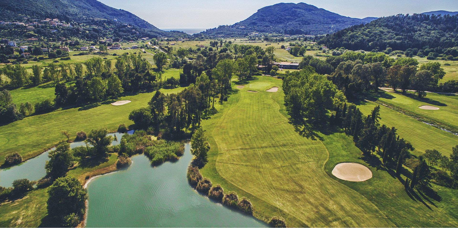 flygvy över golfbana med fairways, bunkrar och vattenhinder omgiven av kullar och träd