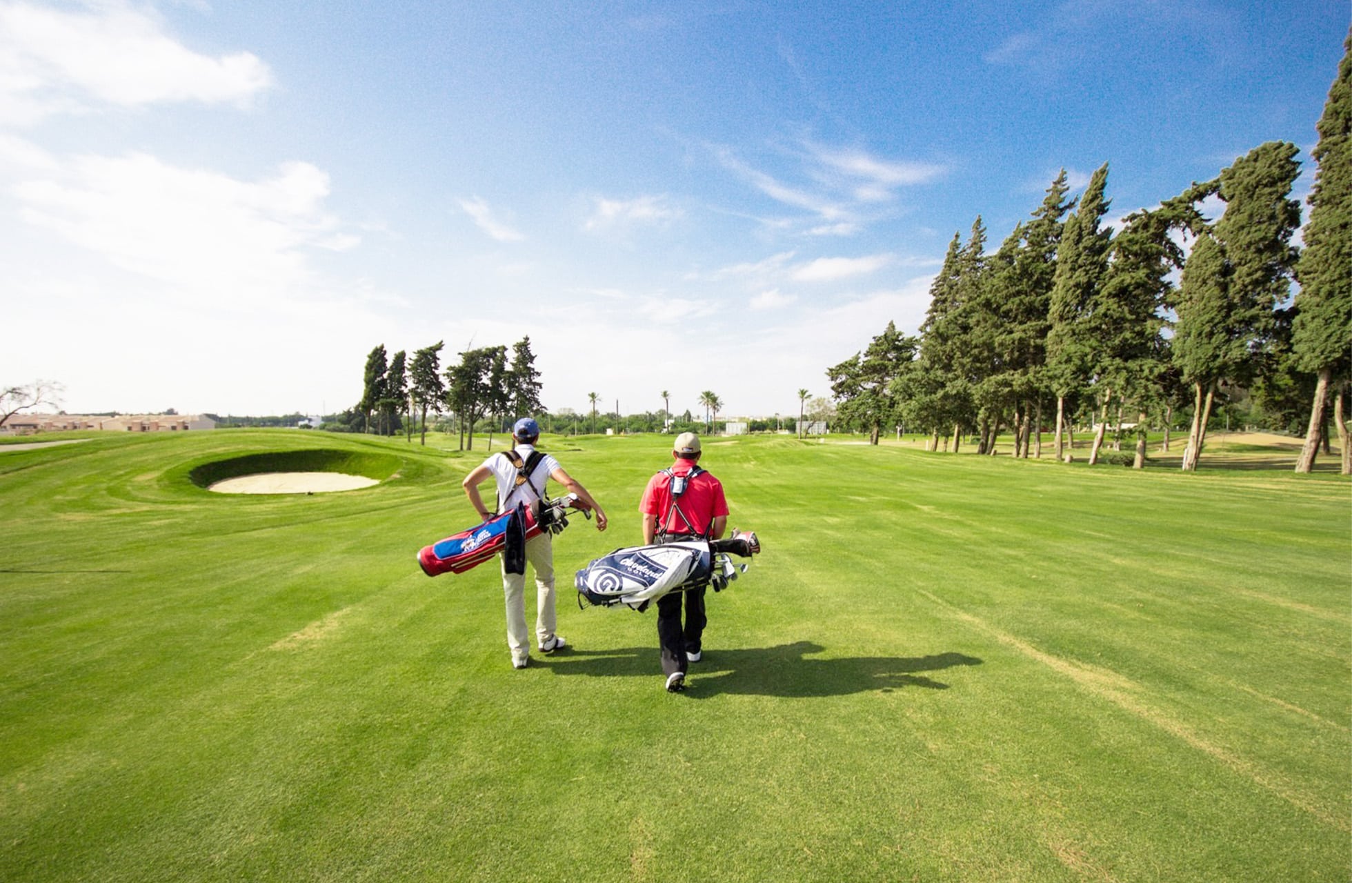 to golfspillere som går på en bred fairway med golfbager under en klar himmel