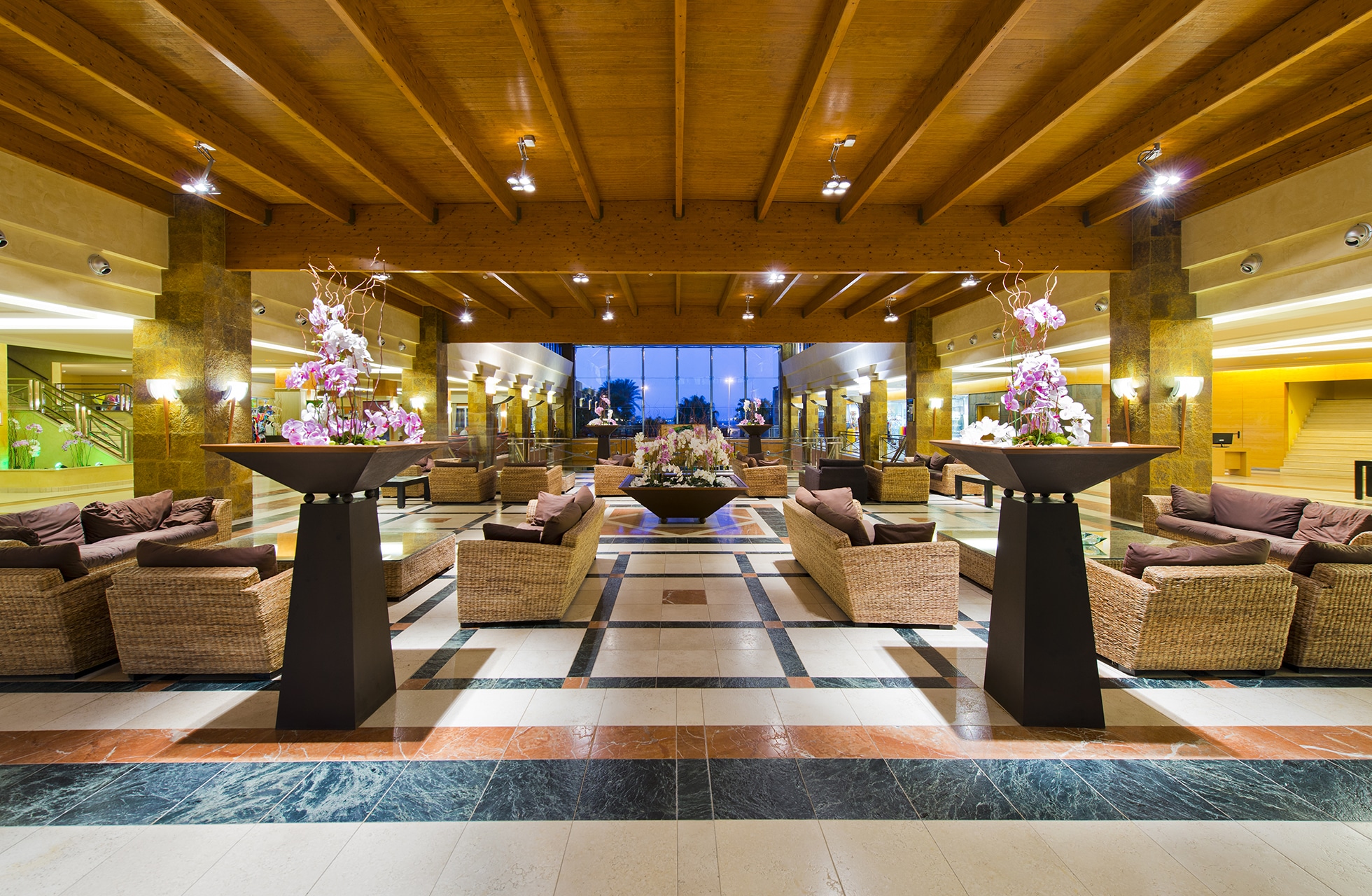 romslig hotellobby med sittegrupper, lenestoler, blomsterarrangementer og tretak i symmetrisk og elegant miljø
