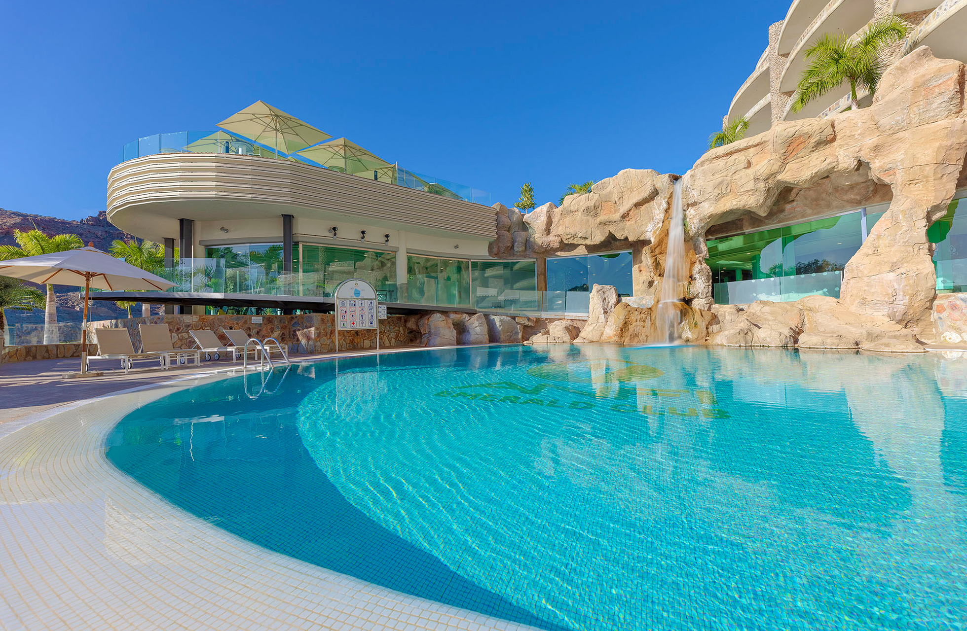laguneformet basseng på anfi emirald club med turkist vann, klippeformasjoner, solsenger og hotellbygning i klart dagslys
