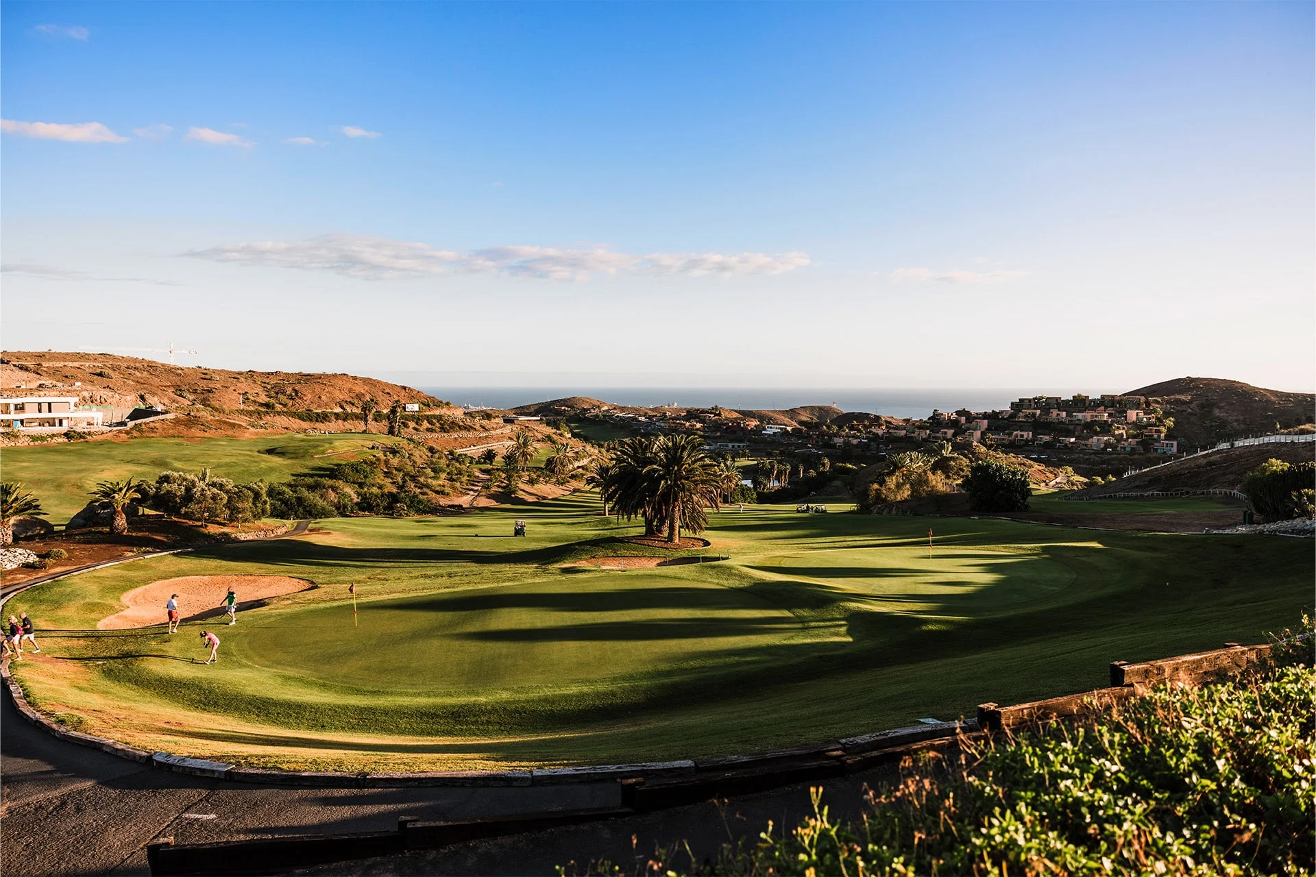 panoramautsikt over golfgreen på salobre golf med golfspillere, bølgende fairway og kupert landskap, med bebyggelse og hav ved horisonten i dagslys