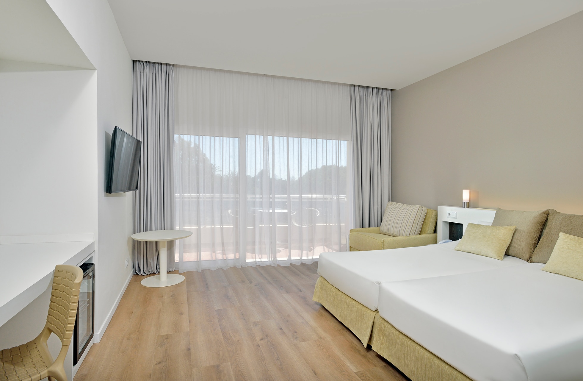 moderne og lyst hotellrom med dobbeltseng, tregulv, skrivebord og store glassdører mot balkong i dagslys