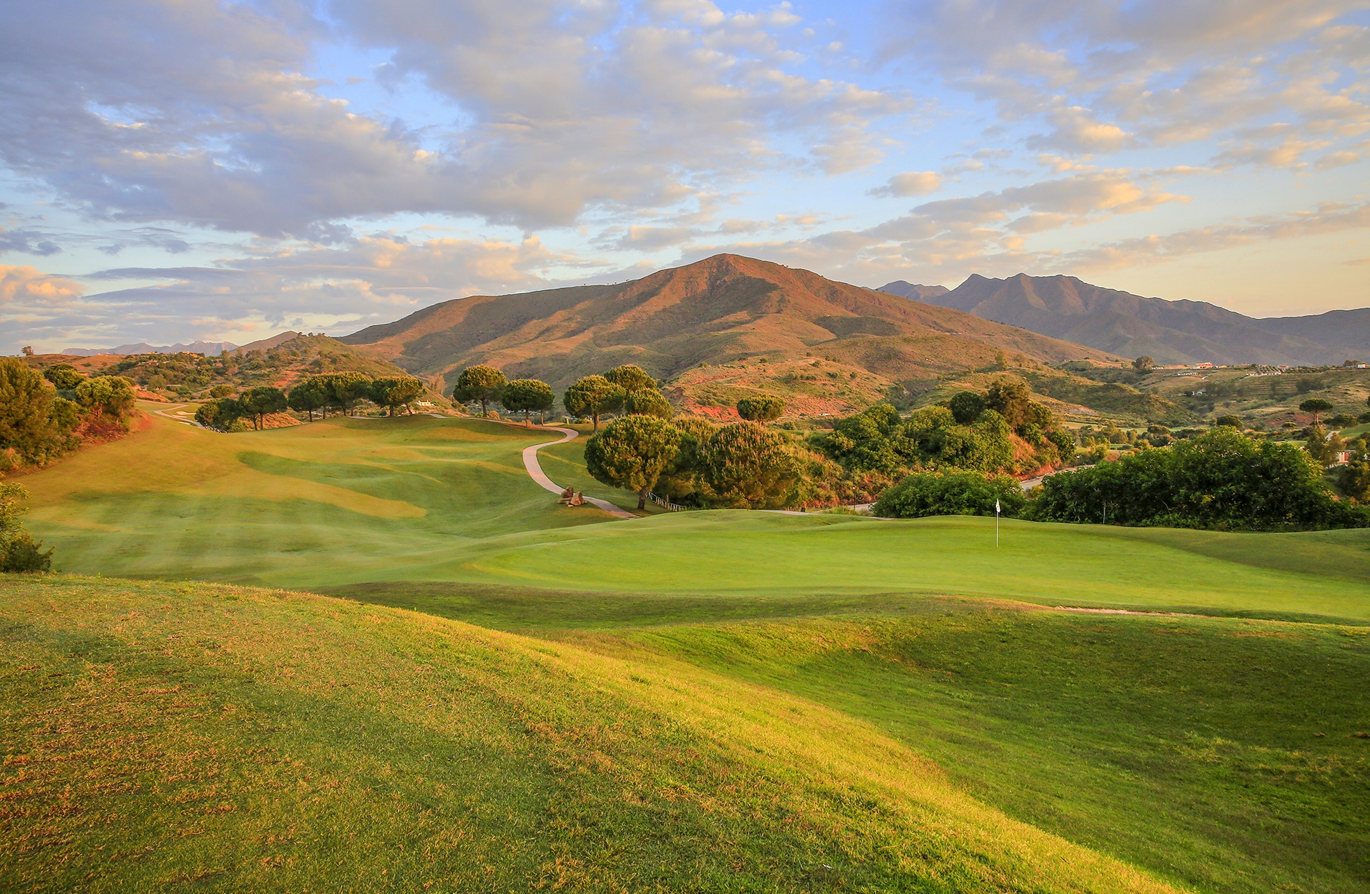 golfbane i kveldslys med fairway, greener og fjell
