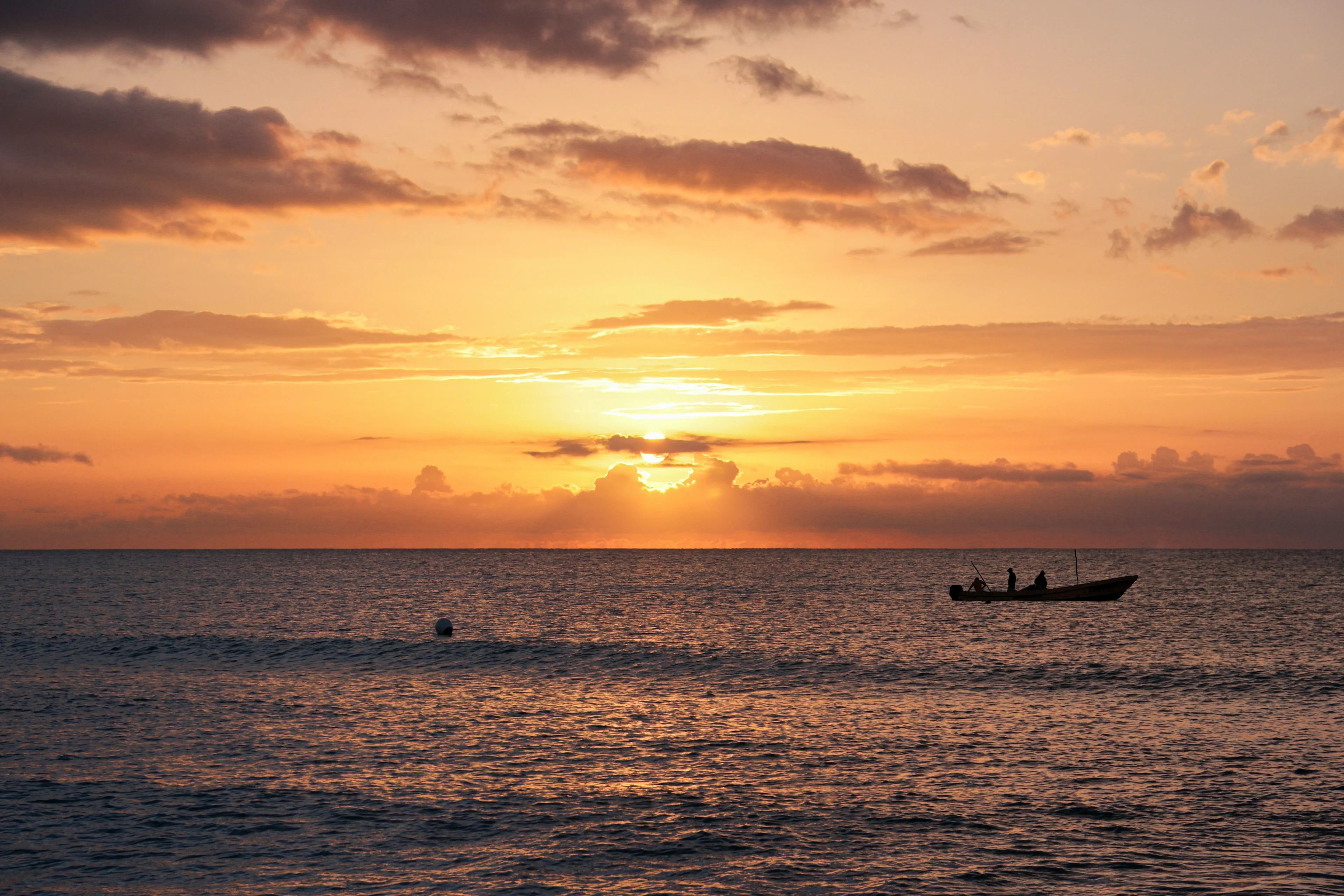 en liten båt med personer er synlig på havet under en fargerik solnedgang