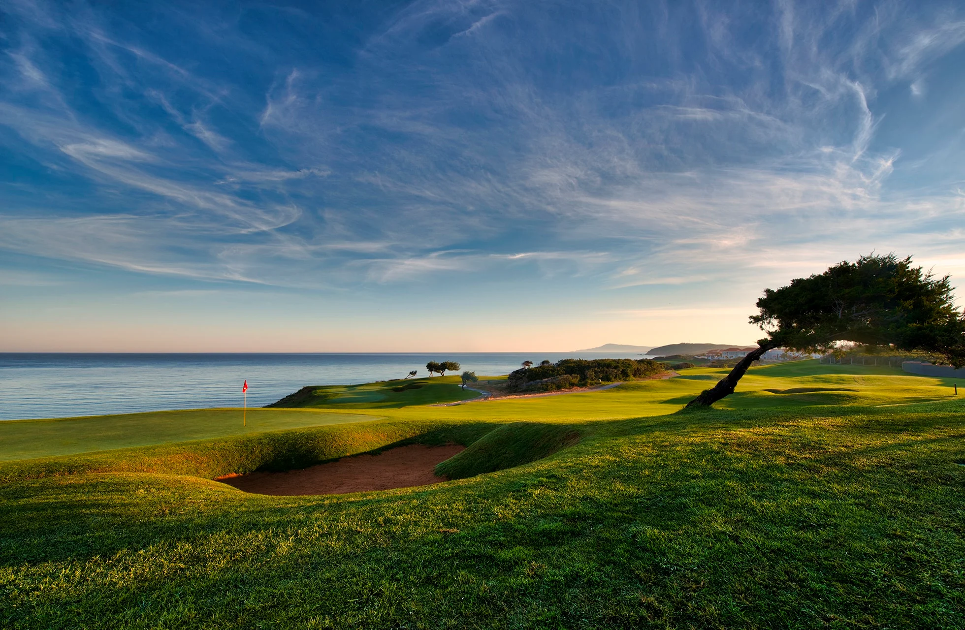kystnær golfbane i tunisien med green og bunker i forgrunnen, havet i bakgrunnen og åpent landskap under dramatisk himmel.