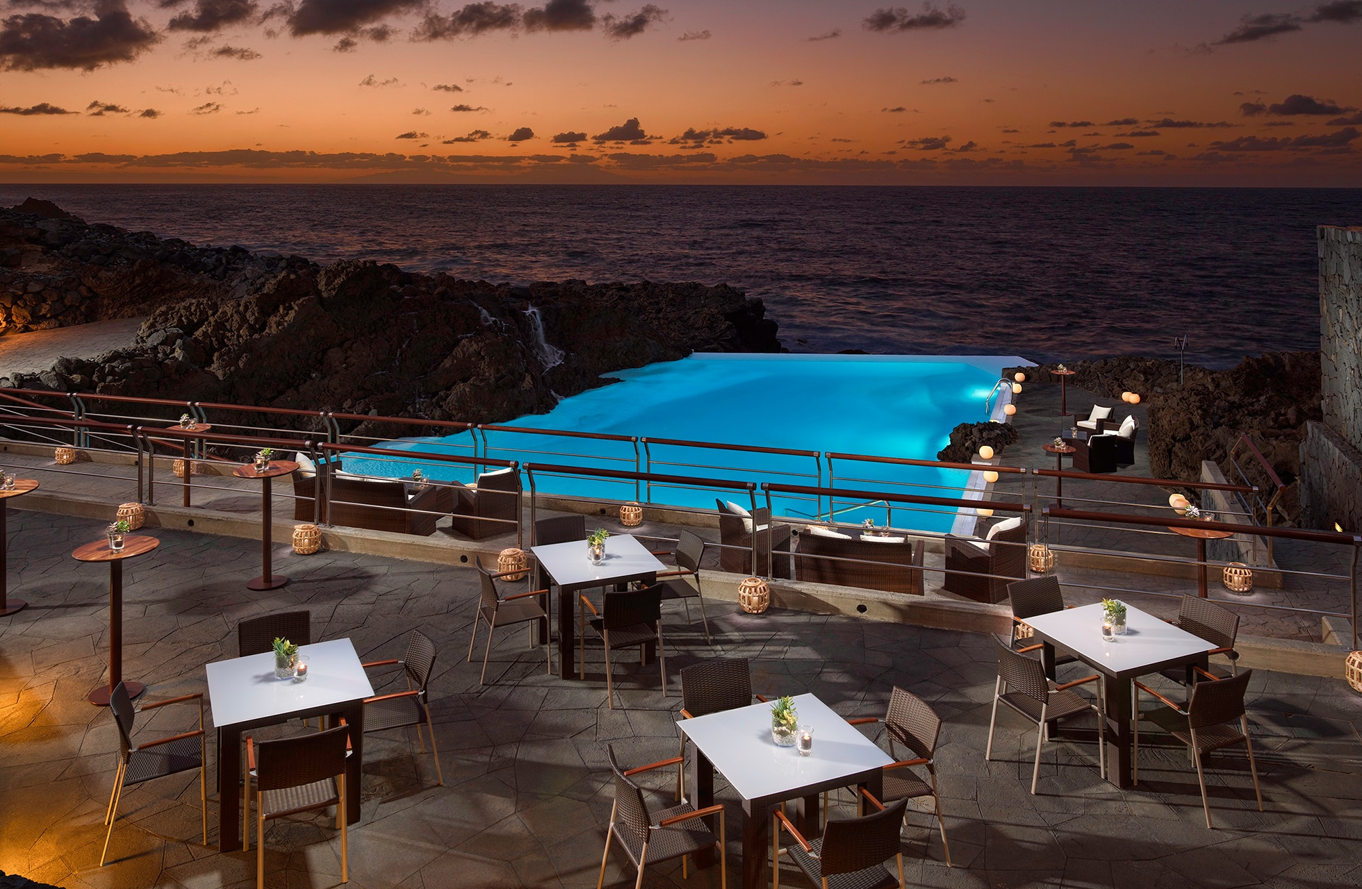 utendørs restaurant på meliá hacienda del conde med dekkede bord på terrasse ved havet, klipper og opplyst basseng i skumringslys
