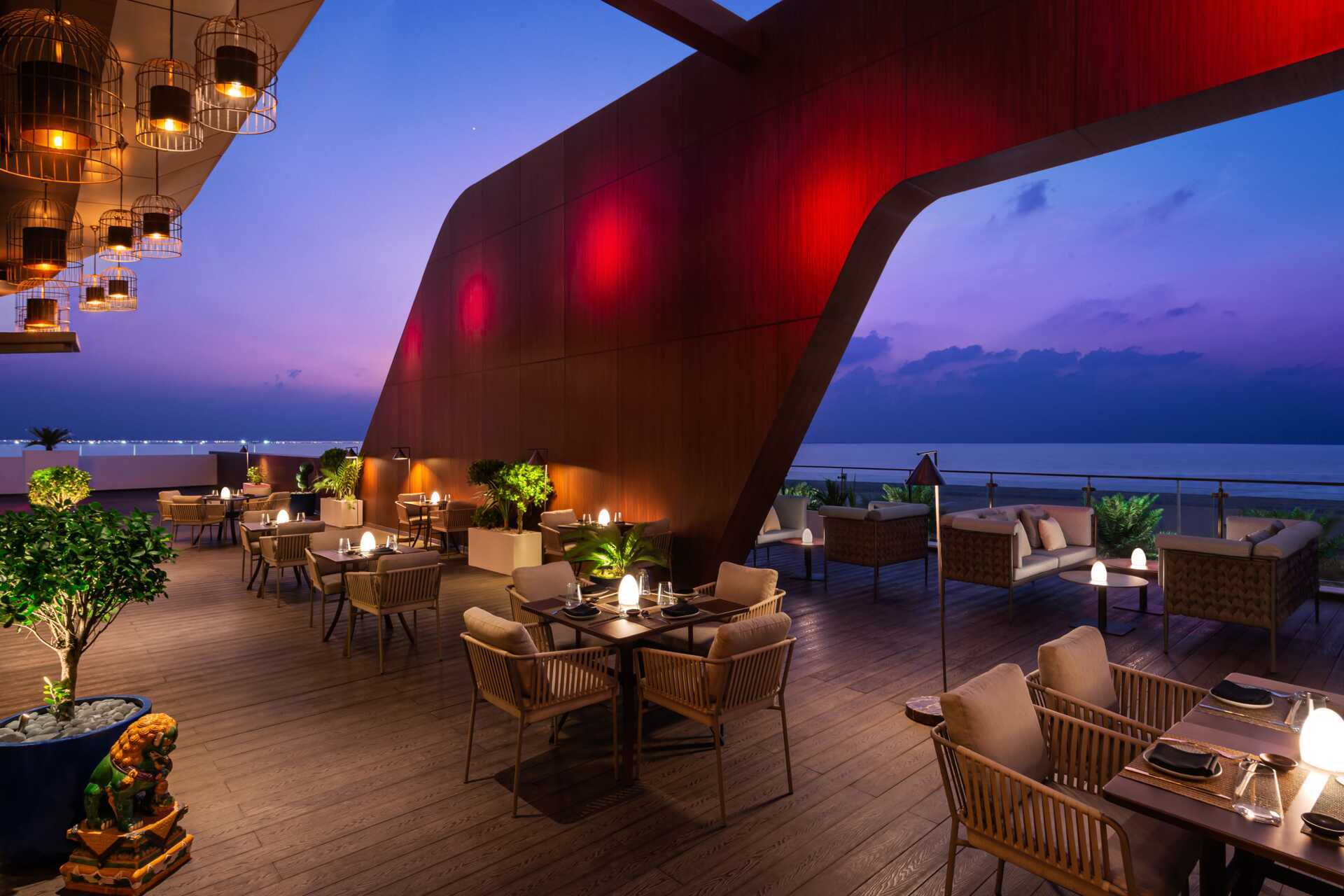Utendørs lounge og restaurant sitteplasser i skumringen med utsikt over havet.
