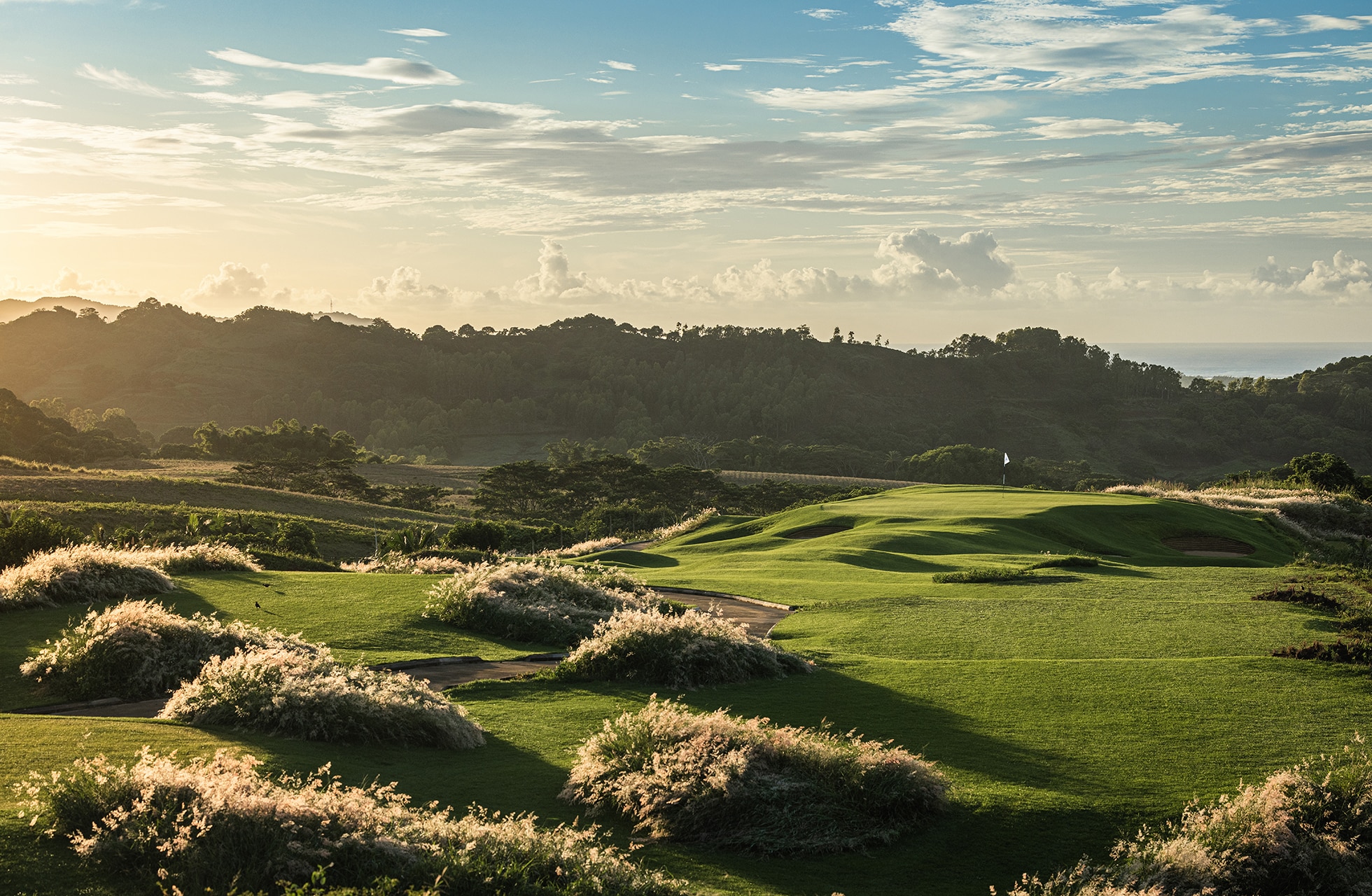 bølgende linksbane på heritage golf club la réserve golf links med grønne fairwayer, naturlig buskvegetasjon og kupert landskap i mykt kveldslys