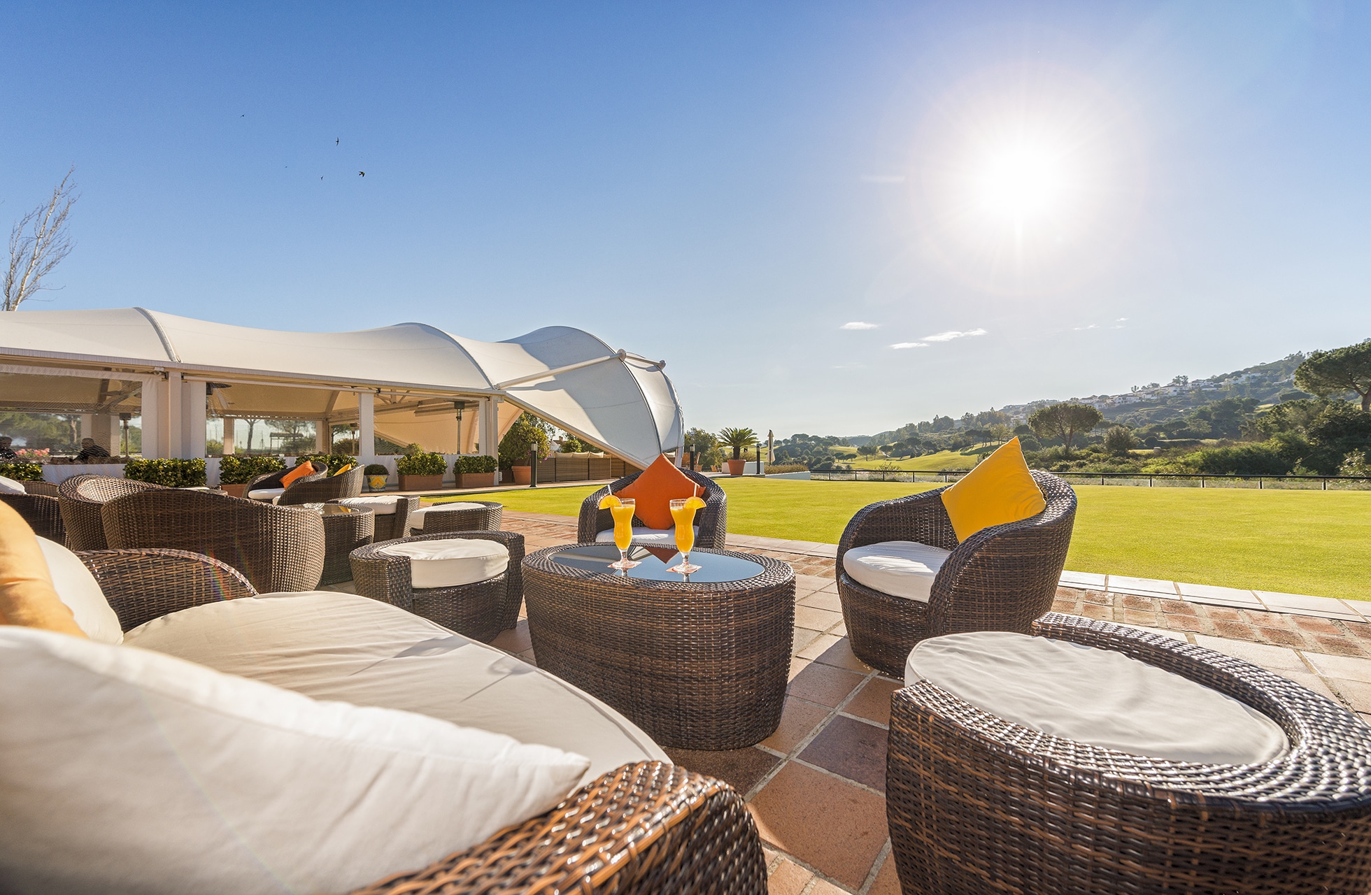 Uteplass med loungemøbler og to drinker med utsikt mot golfbanen.
