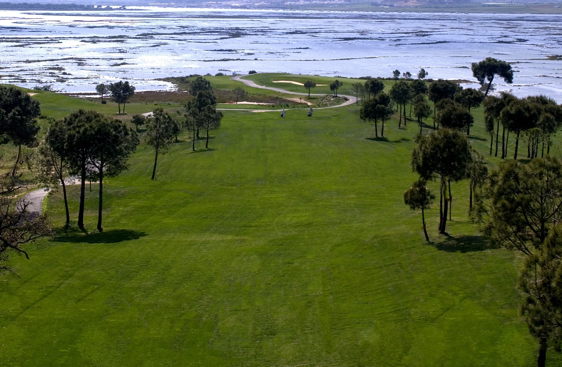 lang fairway med trær langs kantene og utsikt over våtmarker og vann