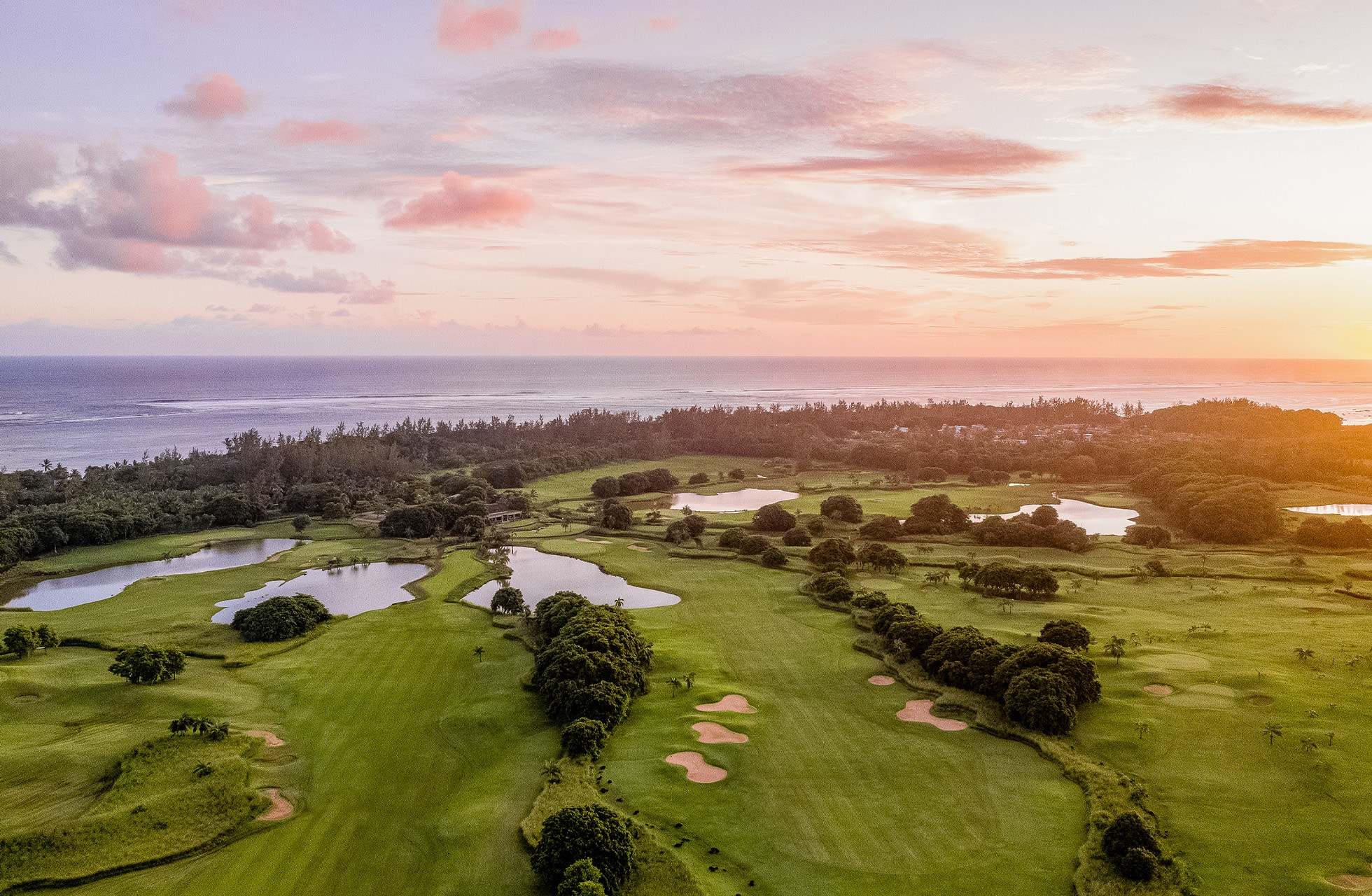 luftfoto af heritage golf club le château med bølgende fairways, vandhazarder og sandbunkere i grønt landskab nær havet i aftenlys