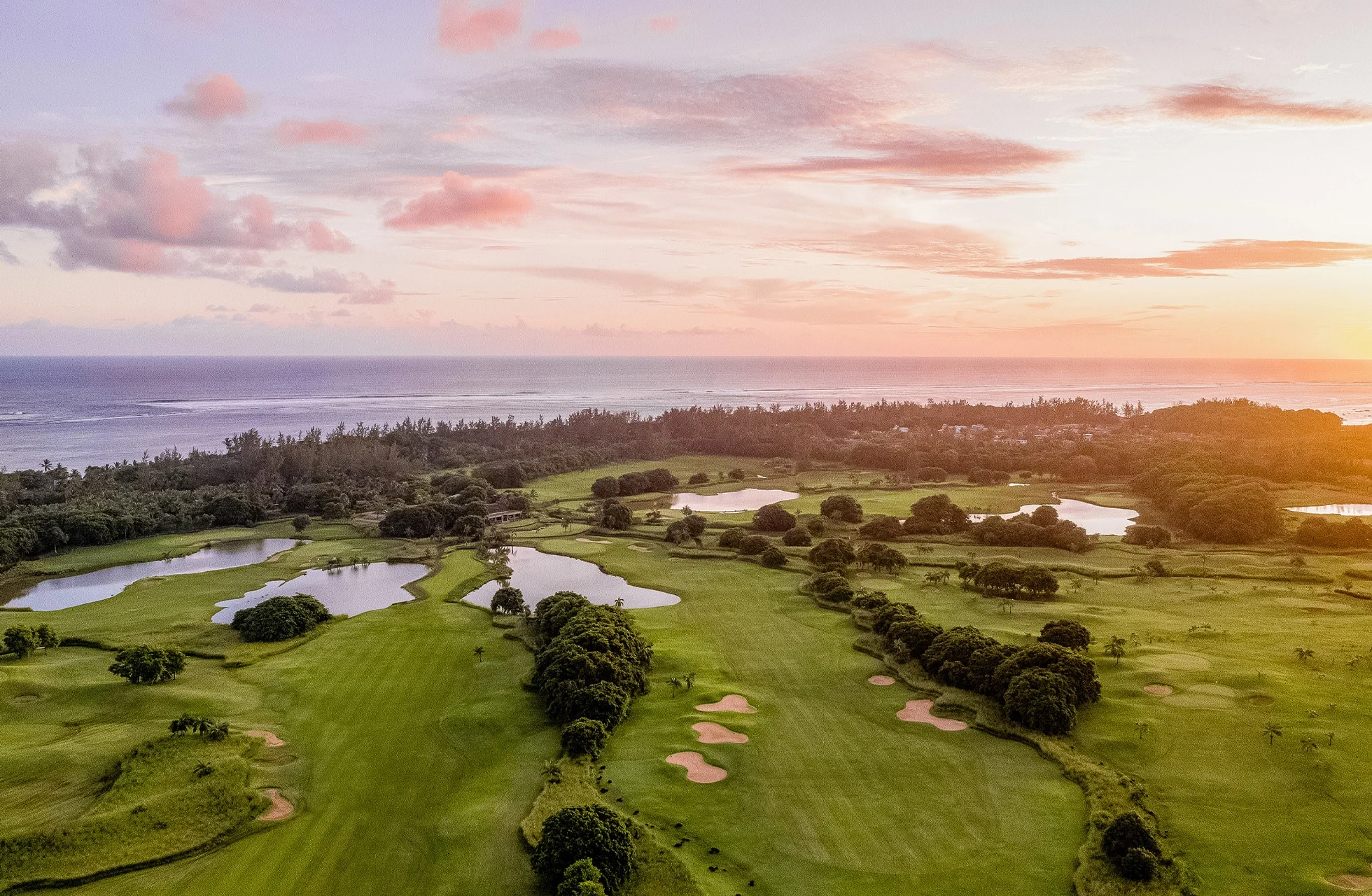 luftfoto af heritage golf club le château med bølgende fairways, vandhazarder og sandbunkere i grønt landskab nær havet i aftenlys