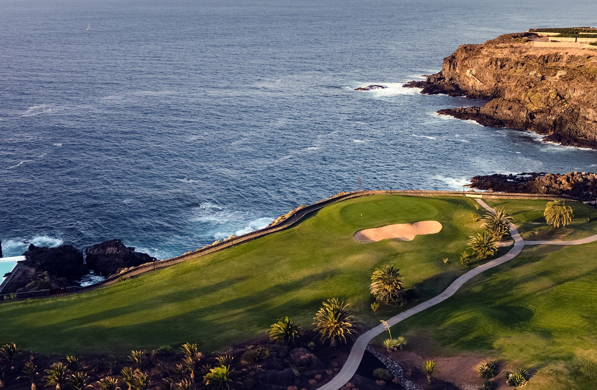 opphøyd green på buenavista golf med bunker og palmetrær, plassert på klipper over atlanterhavskysten