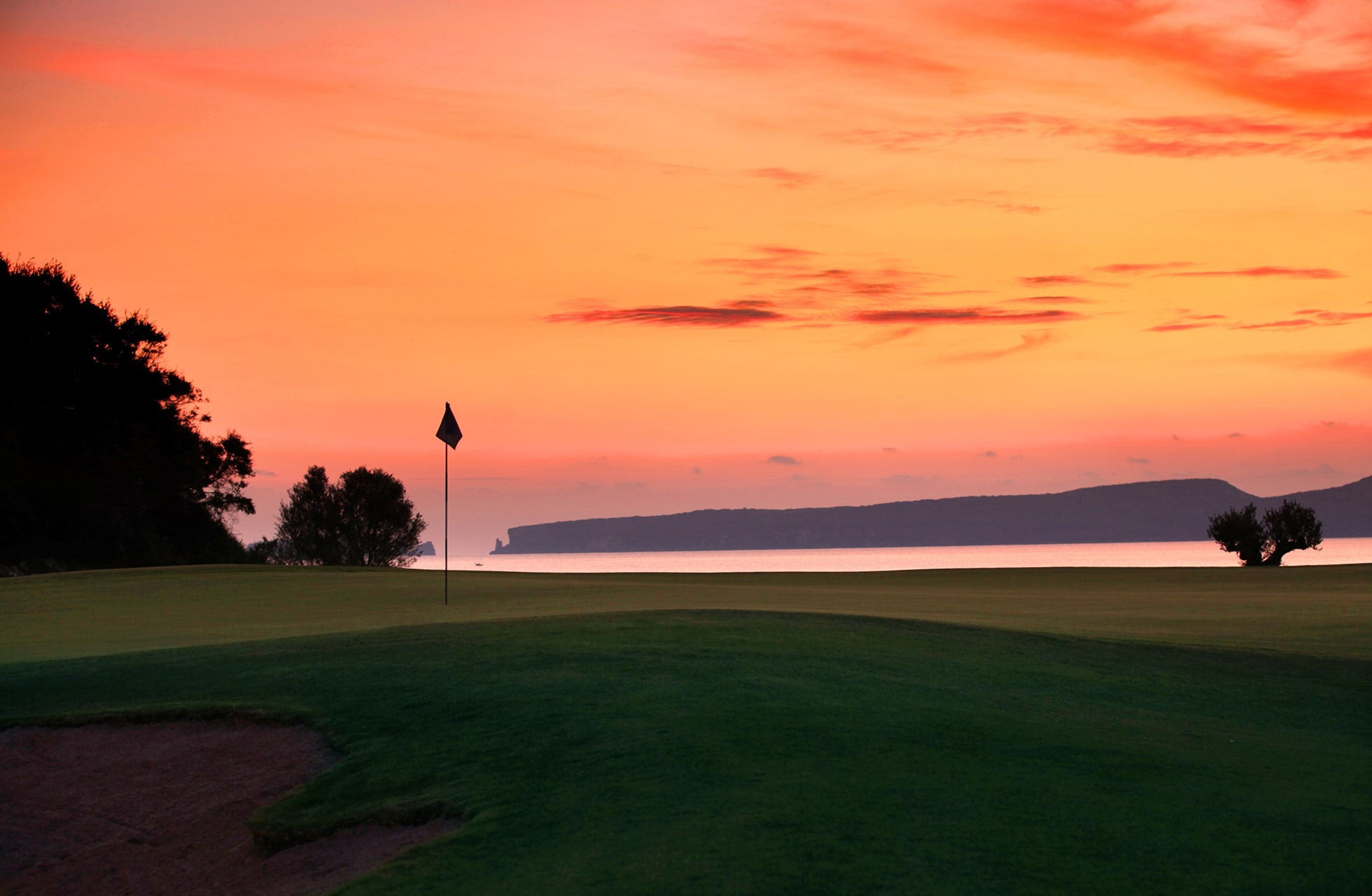 green på the bay course, costa navarino, med flagg i forgrunnen og havet i bakgrunnen i fargerik solnedgang