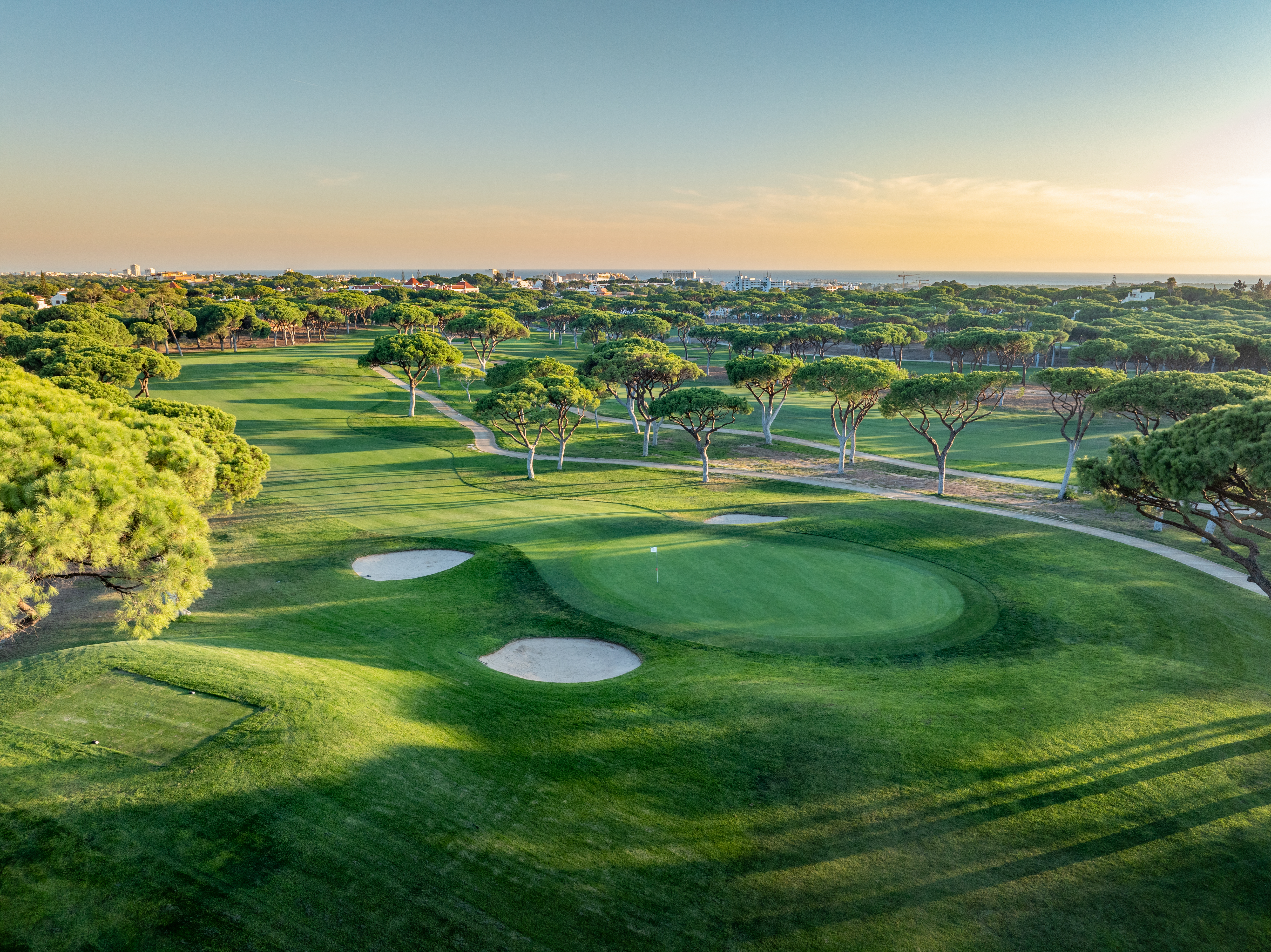 näkymä vihreälle golfkentälle bunkkereineen ja mäntyineen auringon laskiessa