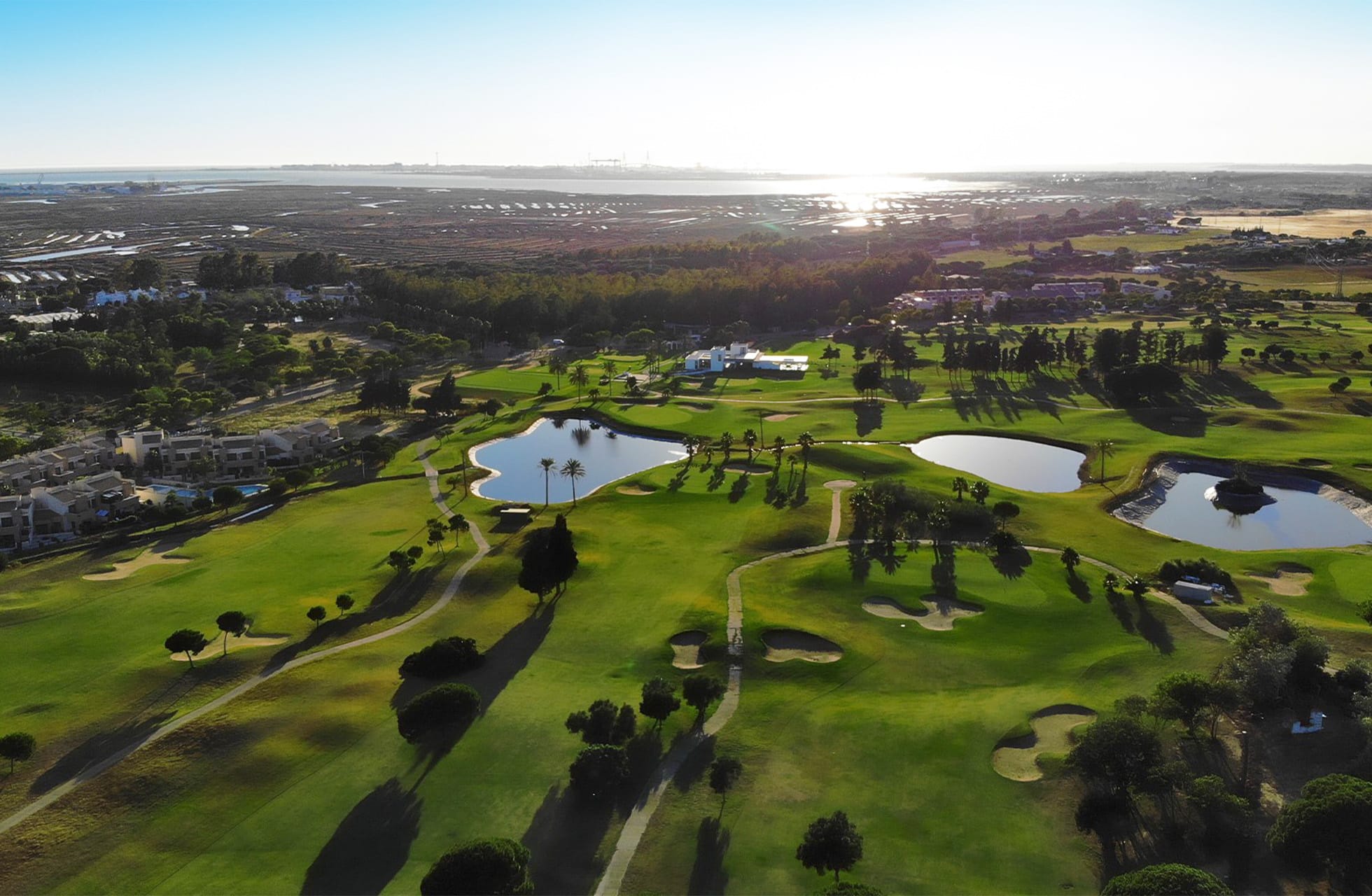 Luftfoto av golfbane med flere innsjøer, palmer og fairways i solnedgangslys