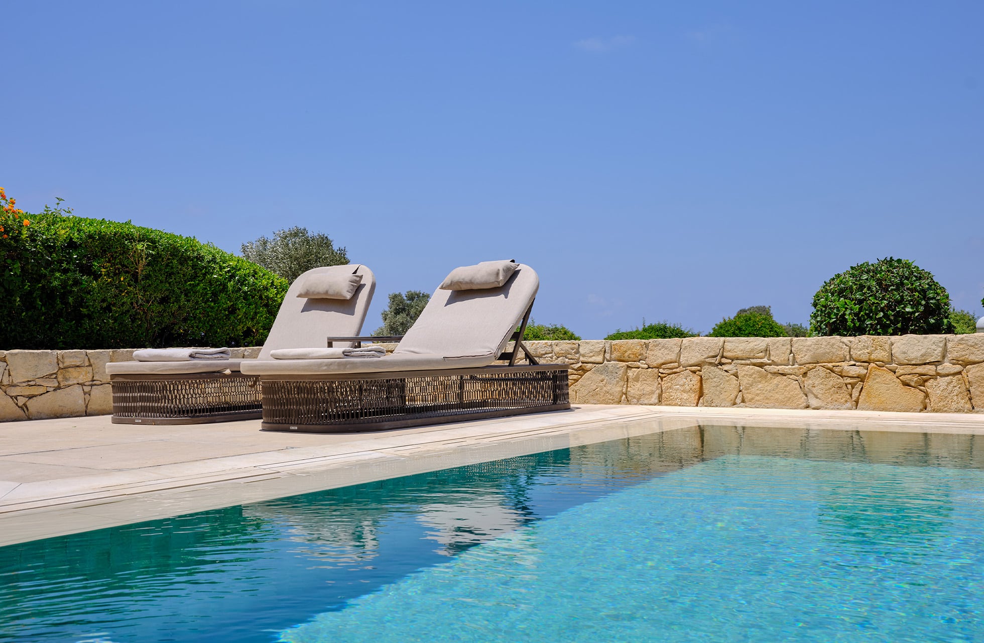 basseng med to solsenger ved aphrodite hills hotel, omgitt av grøntområder og steinmur