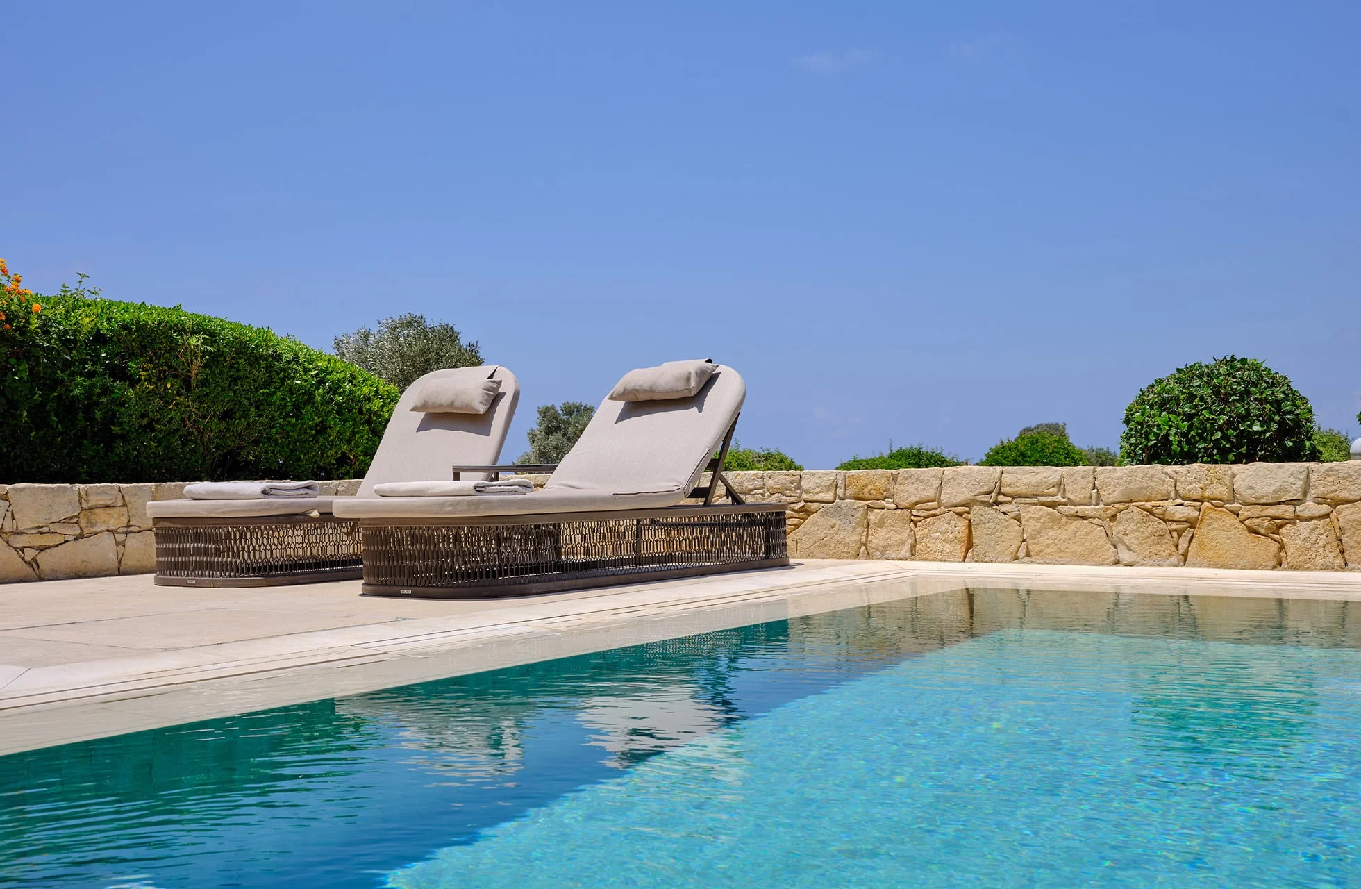 basseng med to solsenger ved aphrodite hills hotel, omgitt av grøntområder og steinmur