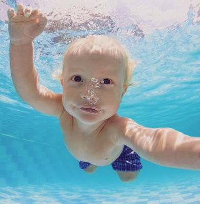 Baby blows bubbles underwater in purified swimming pool waters