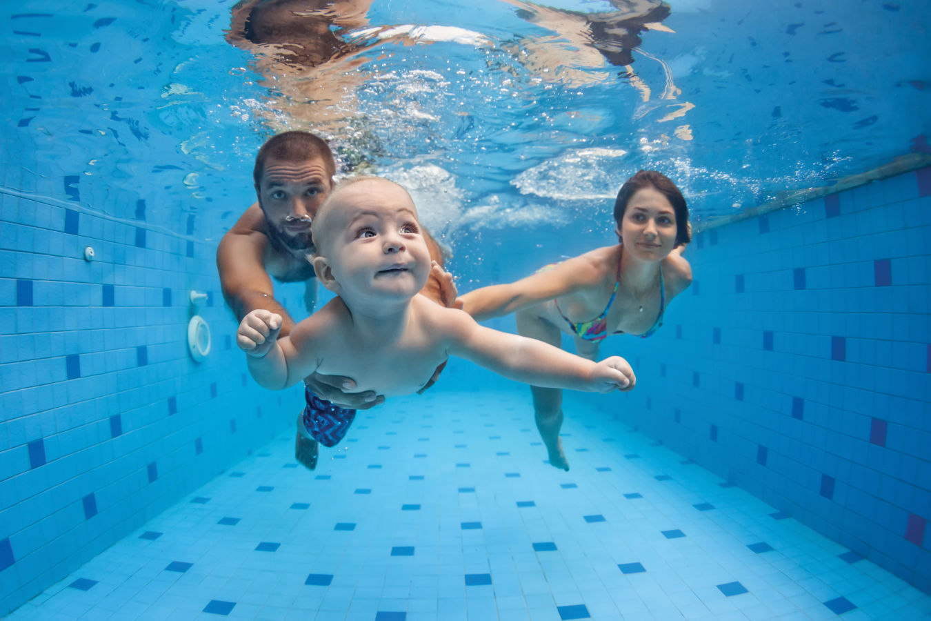 A man, woman and baby swim underwater with their eyes open