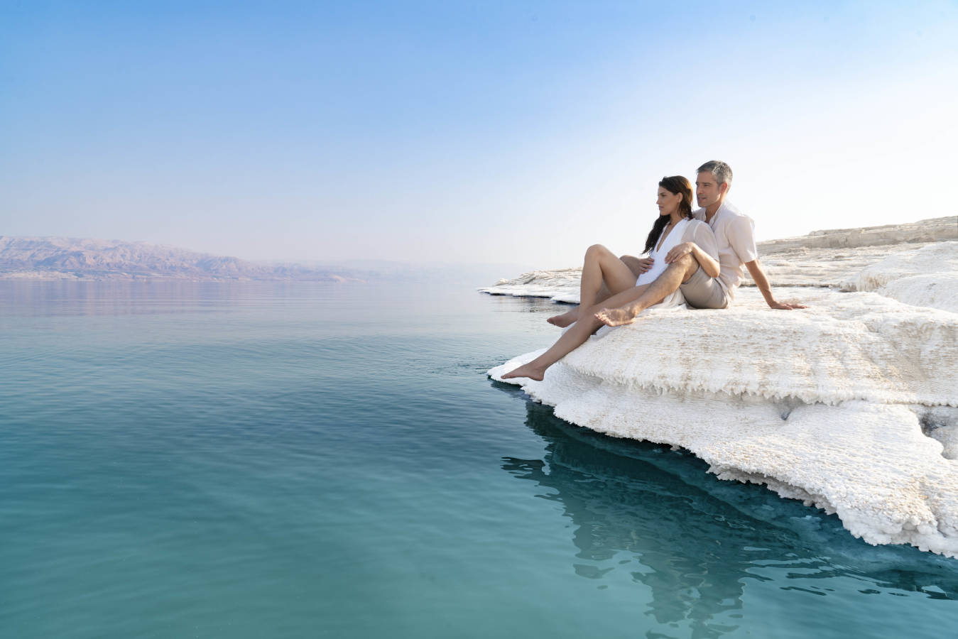 a couple together sitting on salt flat onshore of dead sea