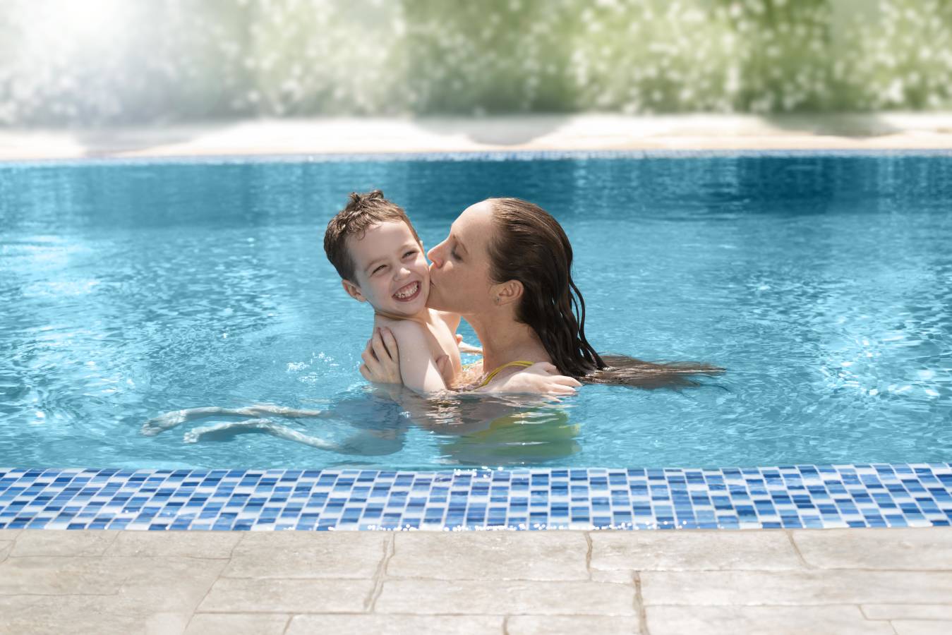 Mother standing in the pool kissing her son on the cheek