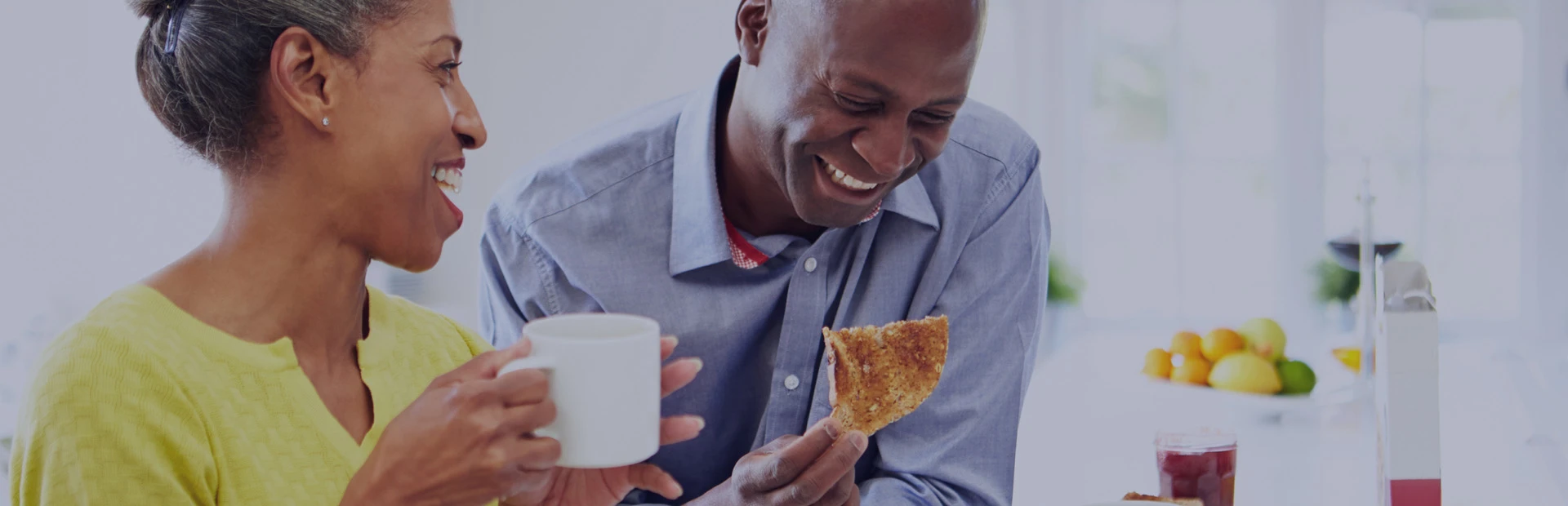 A couple in their 40s are laughing over breakfast as they feel secure in making the decision to choose between dentures or implants thanks to Fixodent. 